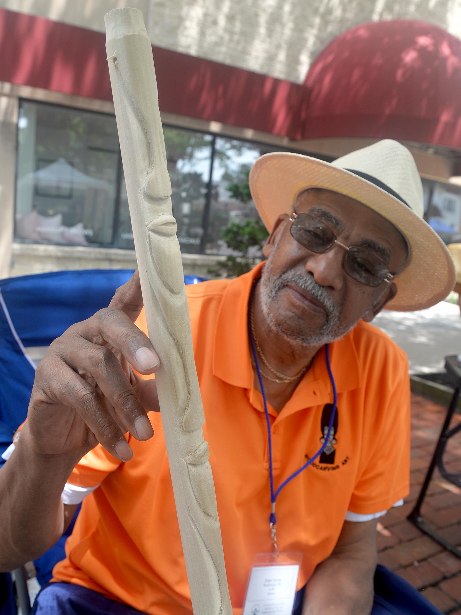 A person shows a wooden walking stick with carved faces on it
