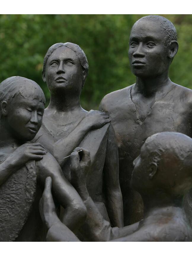 Bronze statue of health worker giving vaccine to one person as two others look on.
