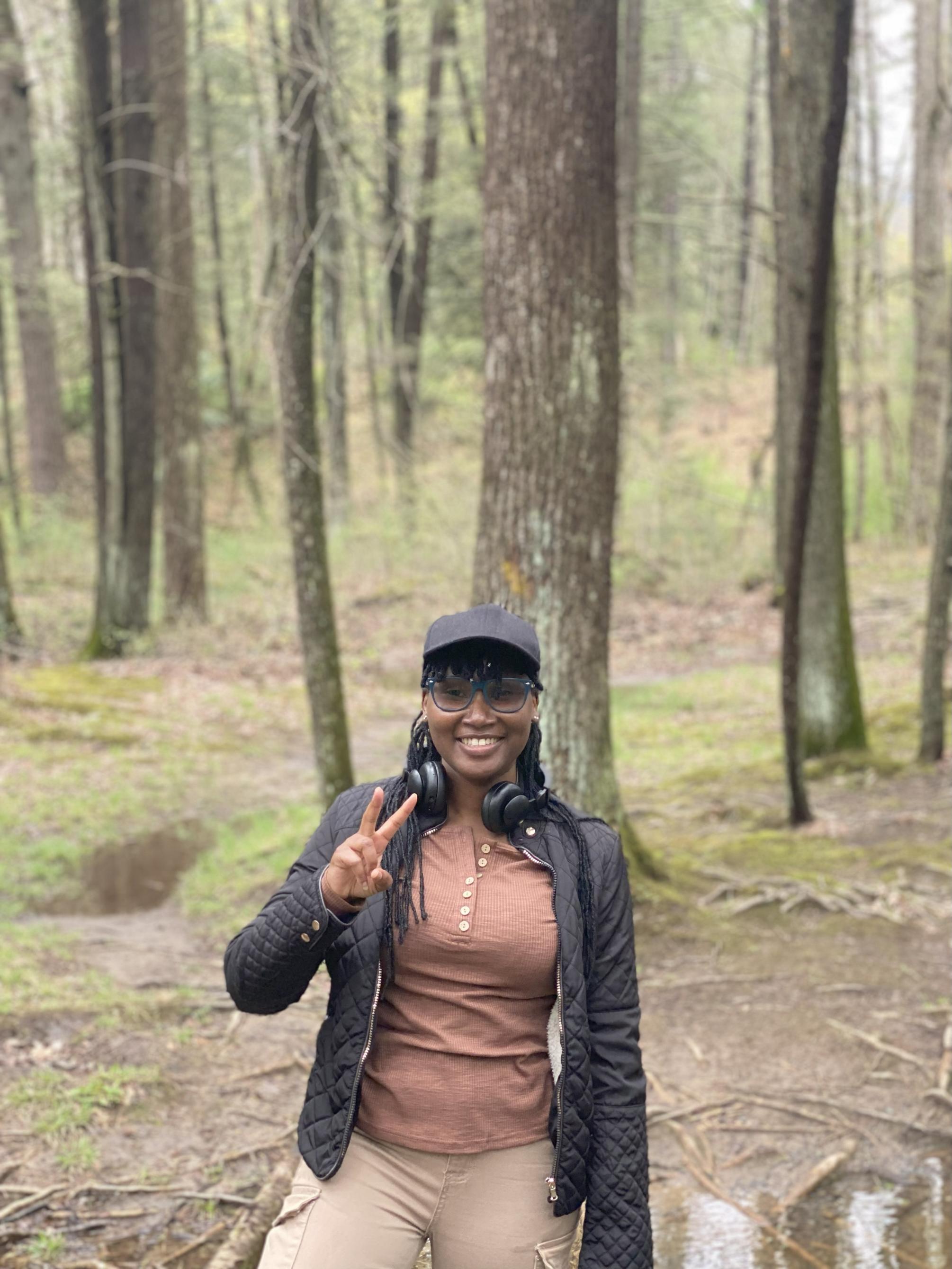 Wilhelmina Antwi displays a peace sign while standing in a woodsy environment. 
