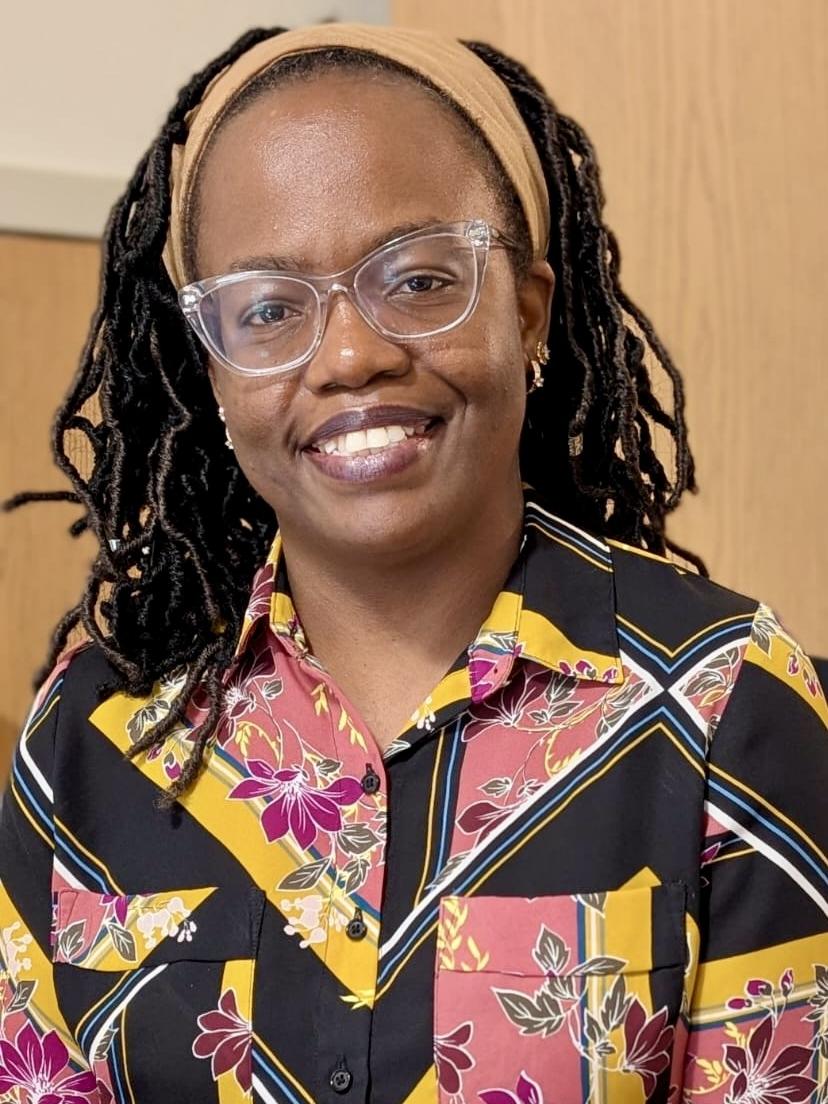 Mercy Muganyizi wears glasses and a black, yellow and pink patterned shirt. 