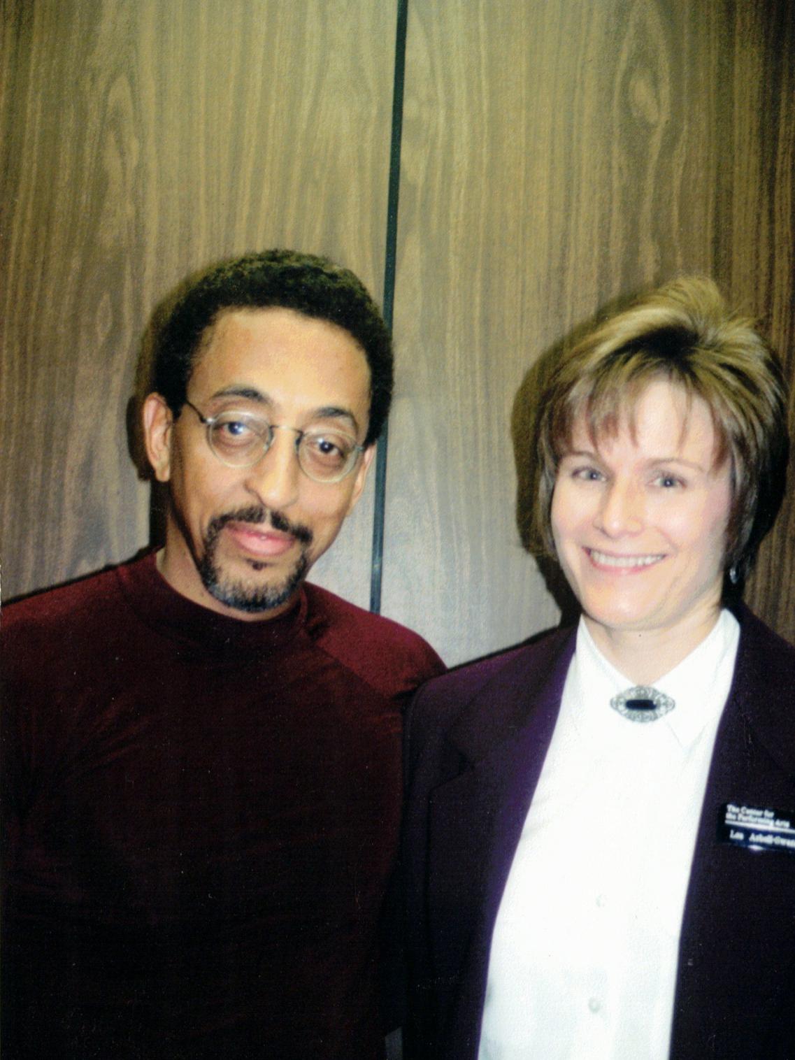 A Black man and a white woman stand shoulder to shoulder and smile.