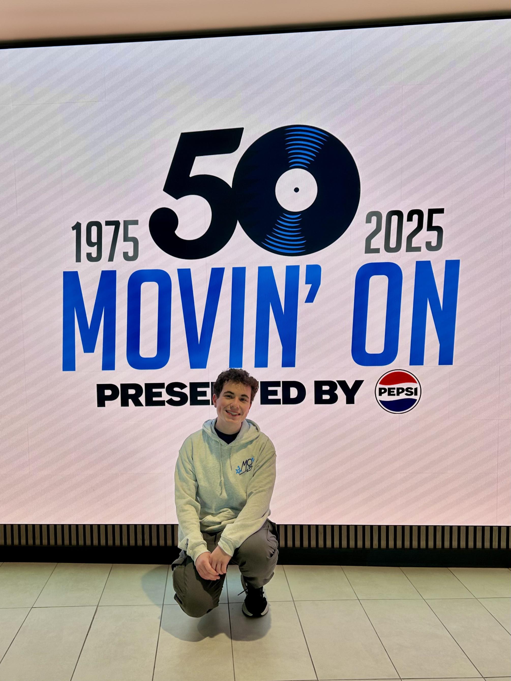 Dominic poses in front of the movin on sign
