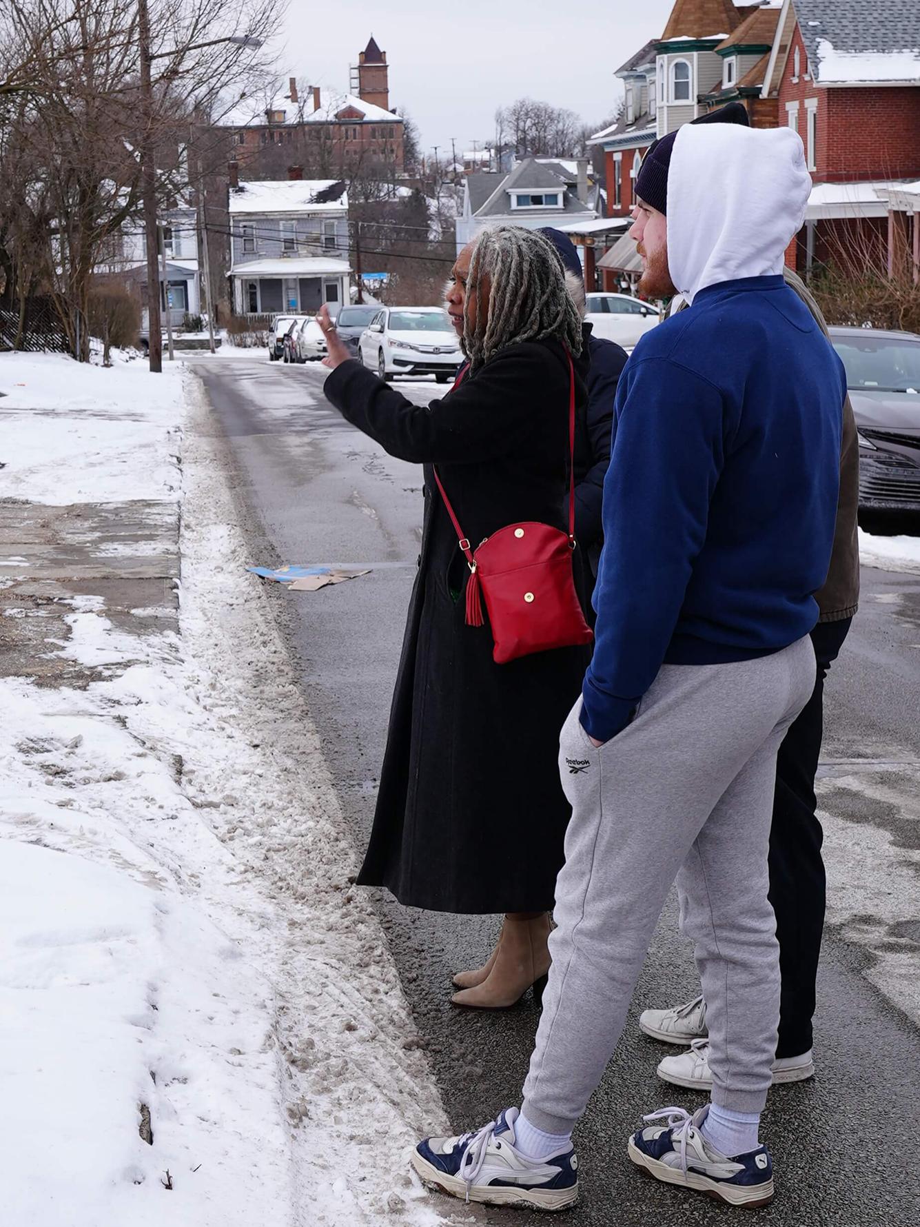 Two adults standing on a street in the snow pointing at something outside of the photo.