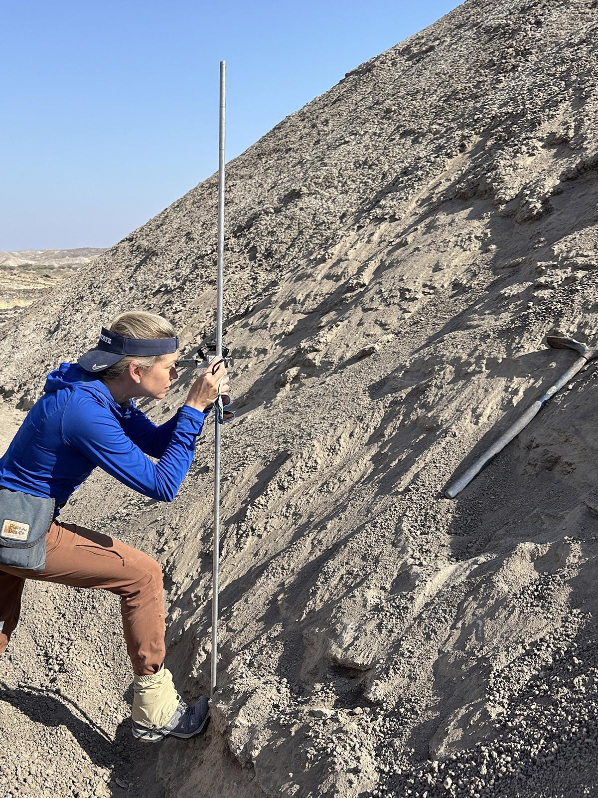 Erin DiMaggio uses a jacob staff to measure the thickness of rock layers.
