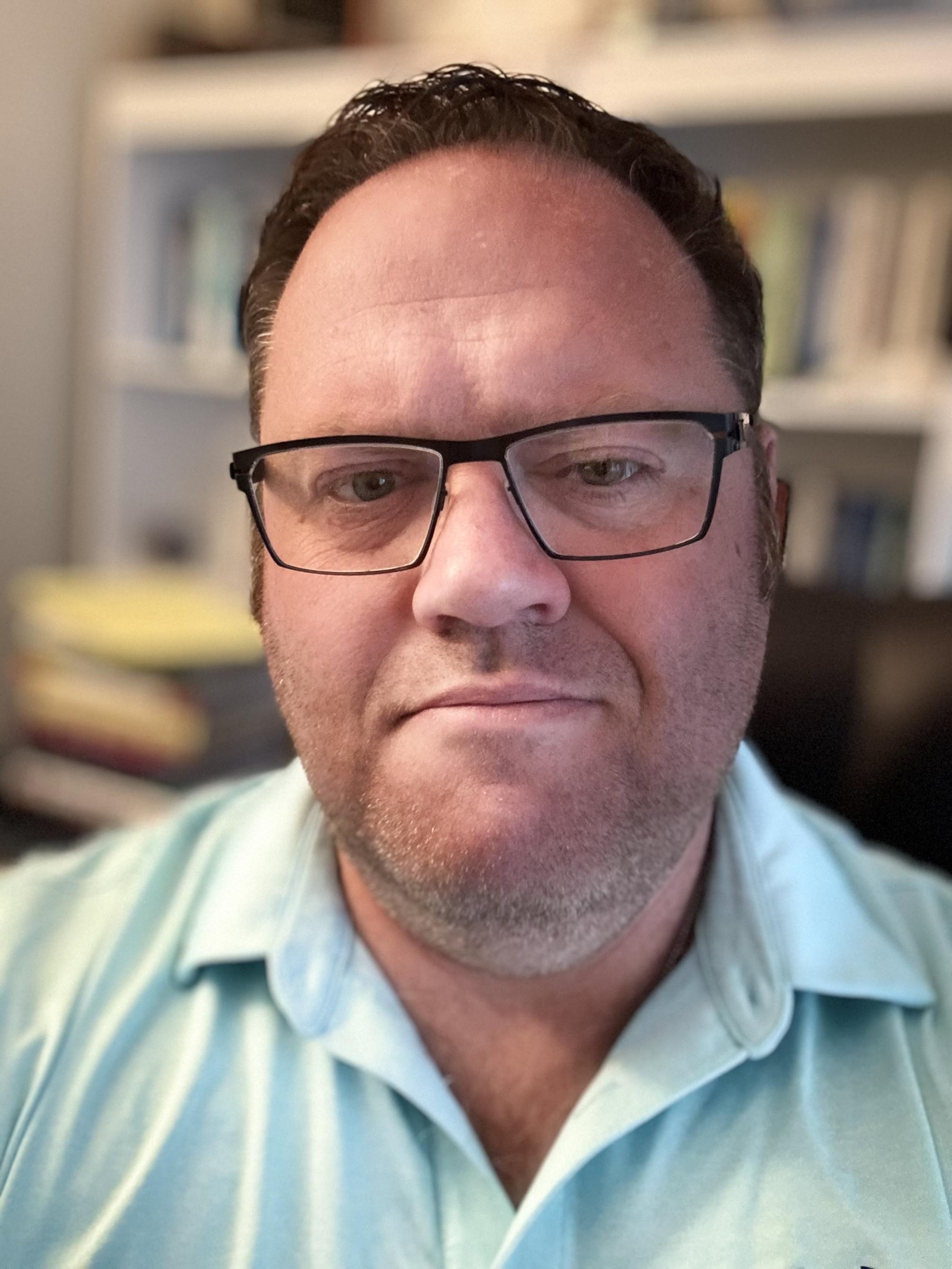 Michael Putnam wearing glasses with a bookshelf behind him 