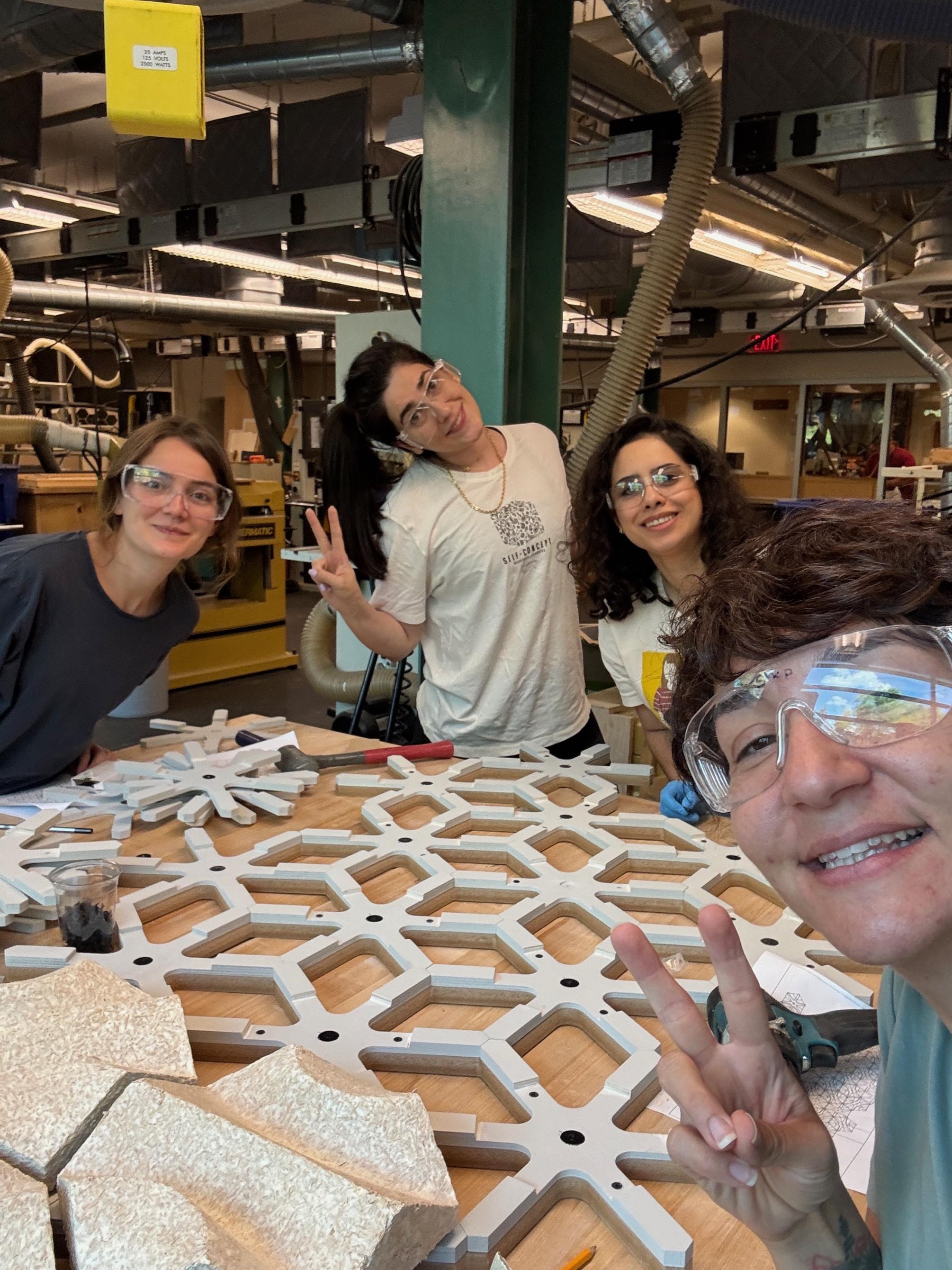 Four individuals pose around a wooden structure on a table in a workshop.