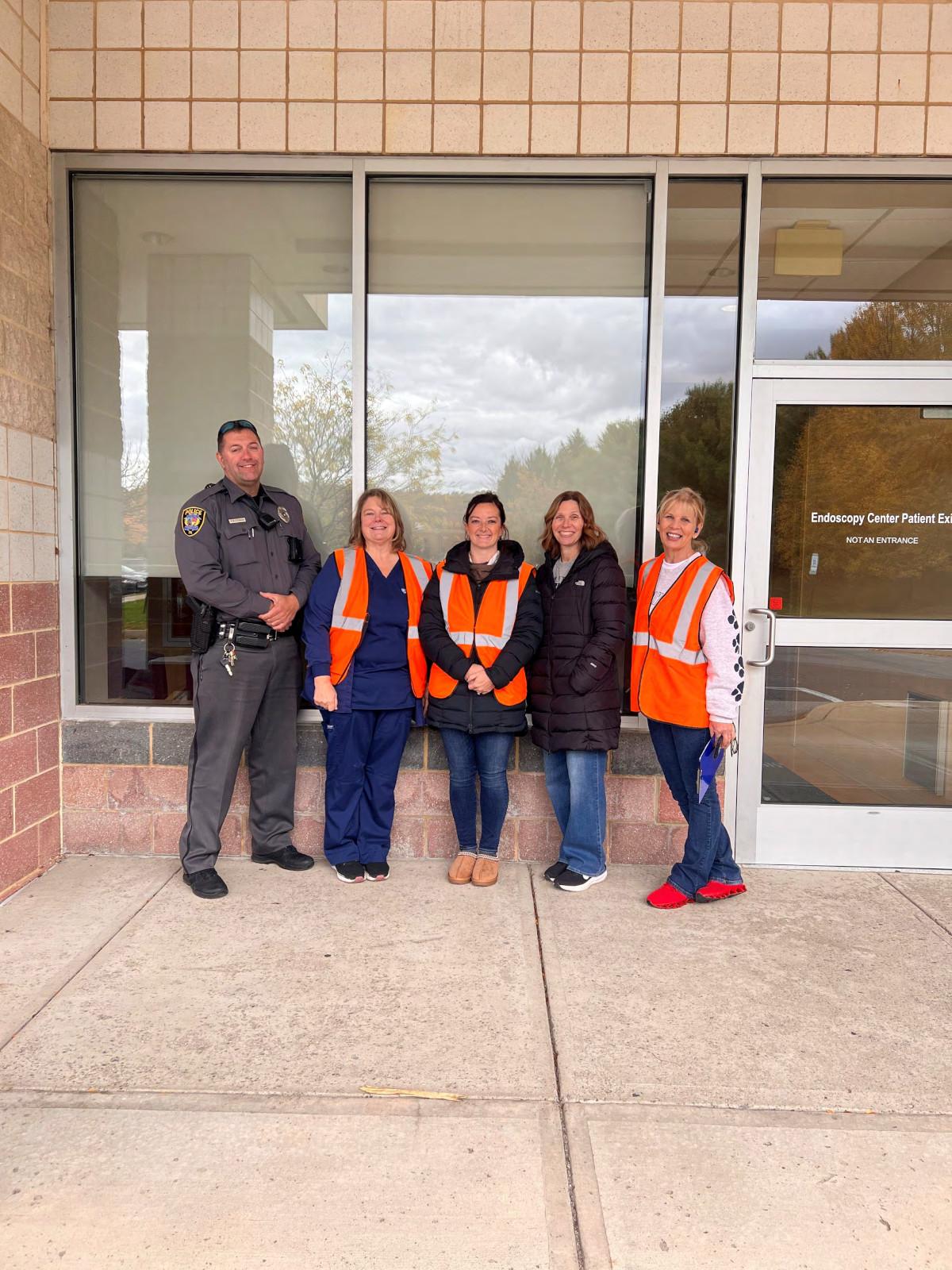 Five adults stand in a row outside a building entrance.
