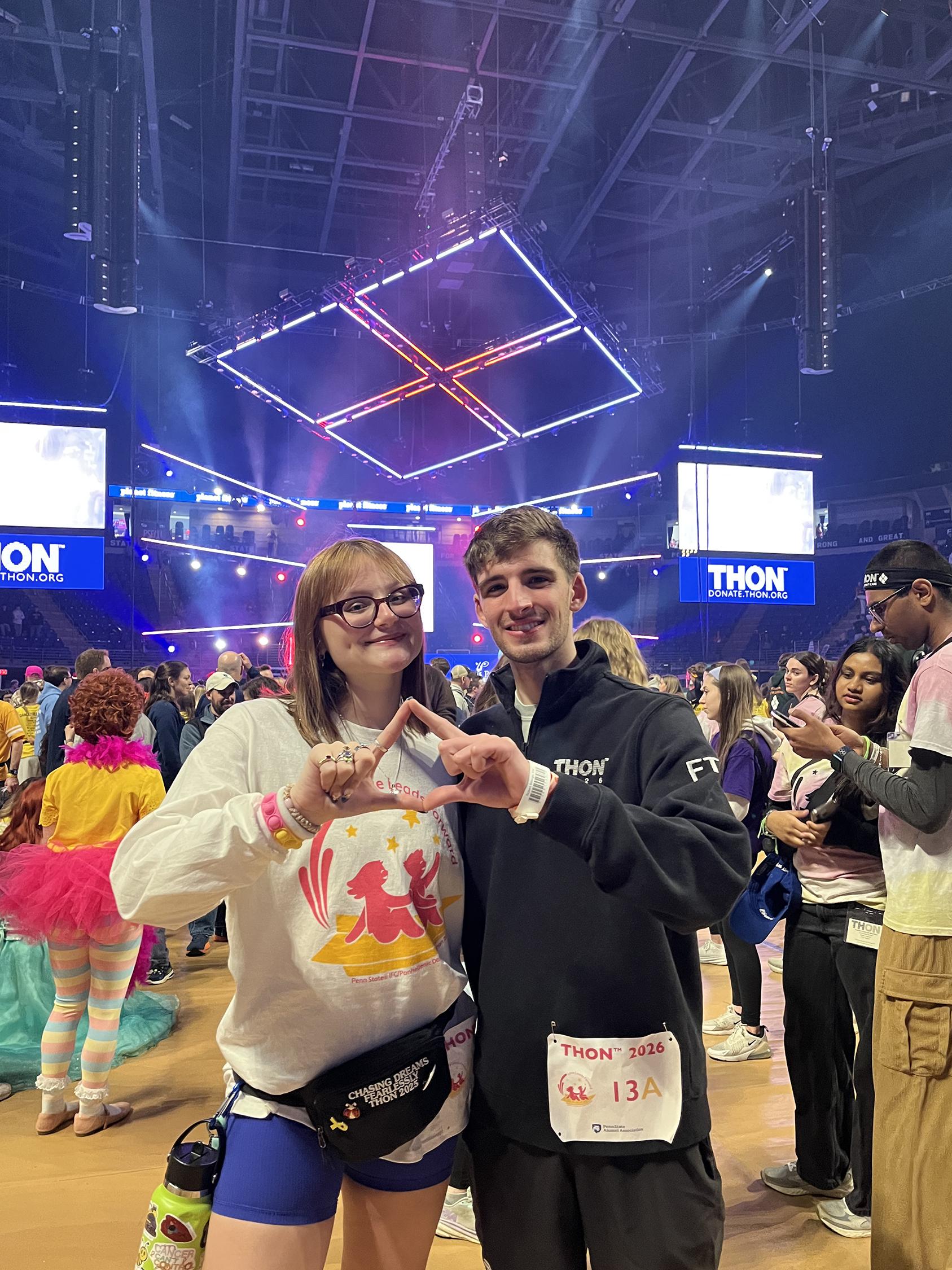 Two people pose in front of a stage inside an arena.