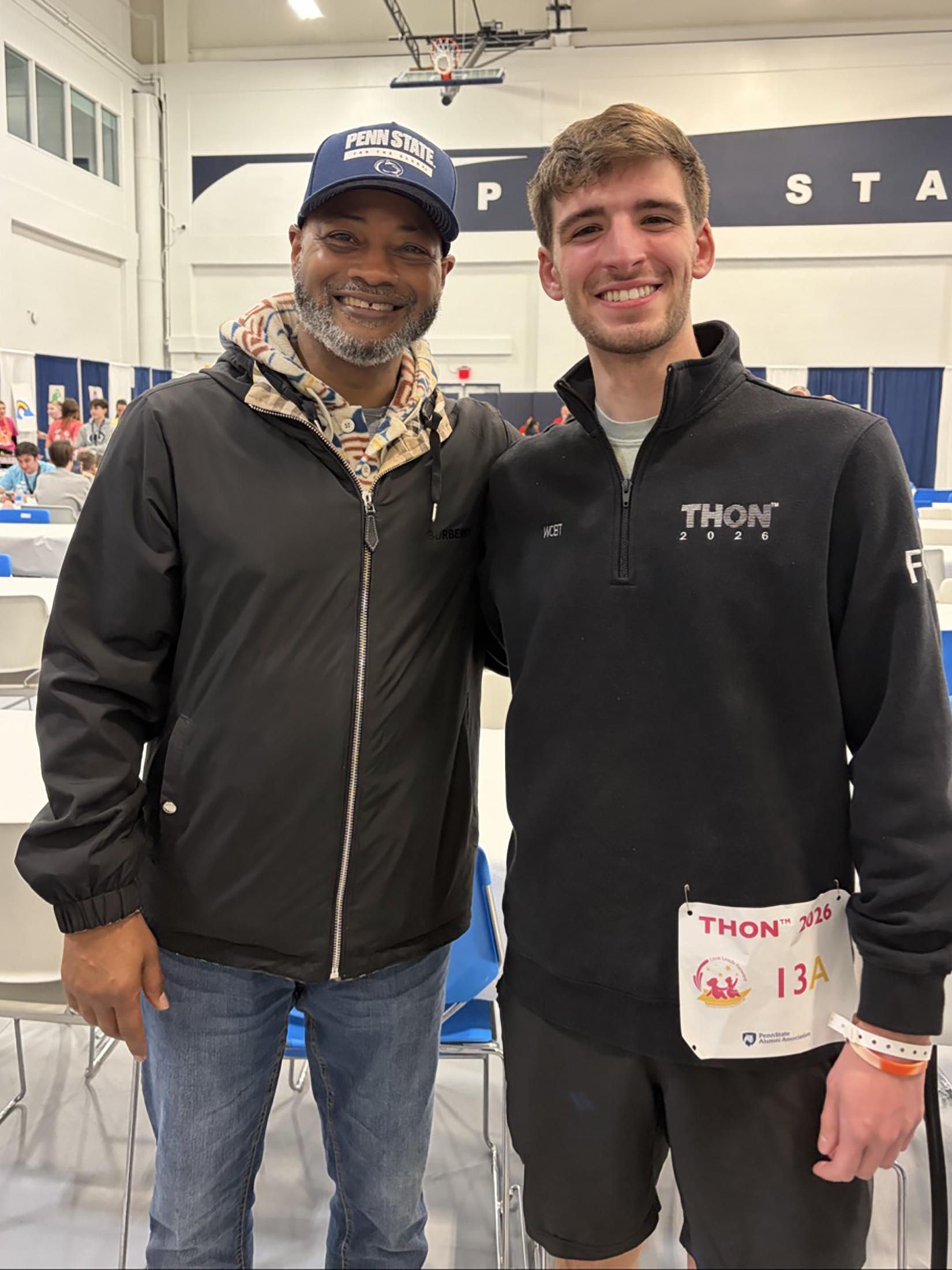 Two men pose for a photo in a gym.