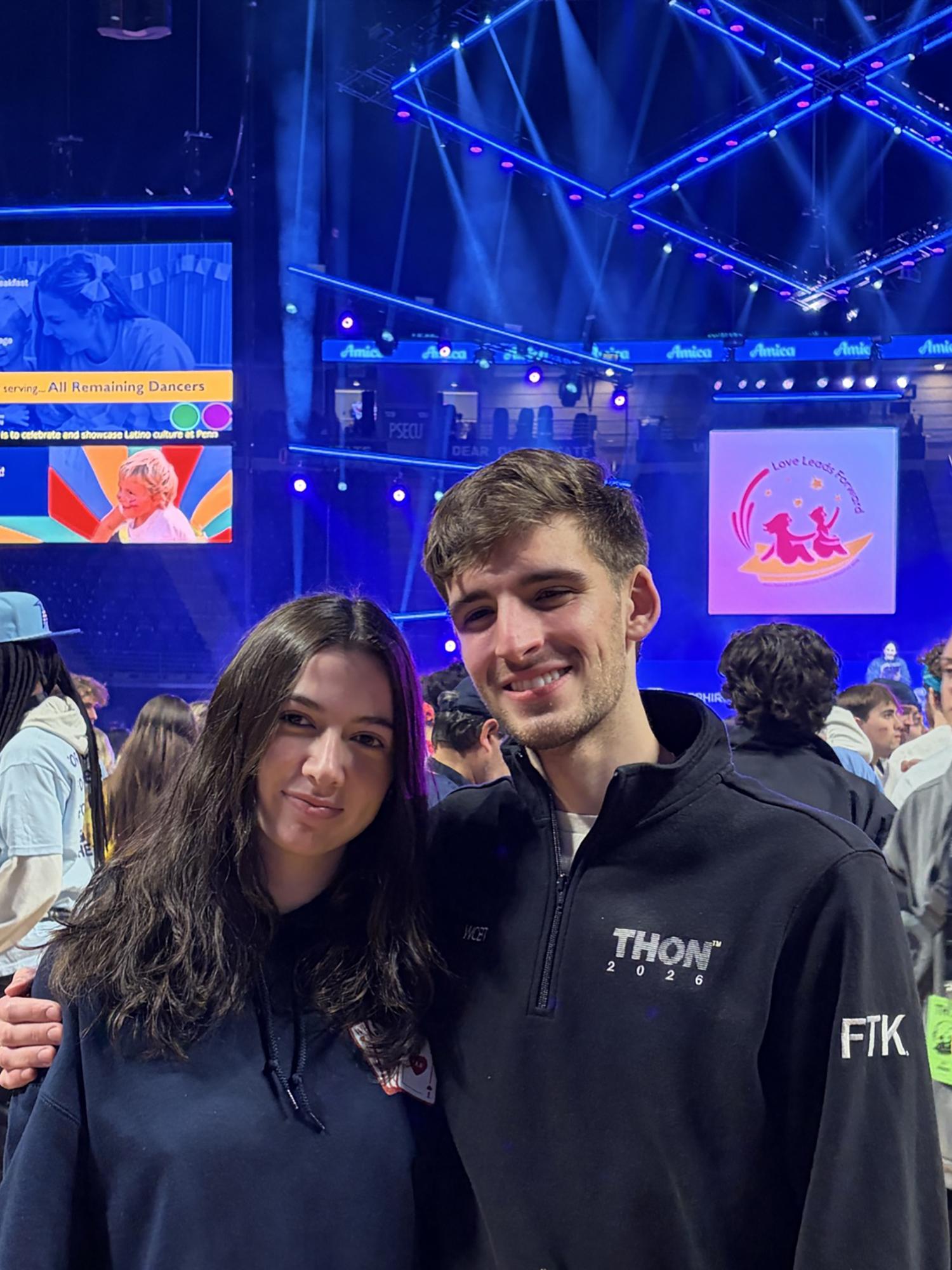 Two people pose in front of a stage inside an arena.
