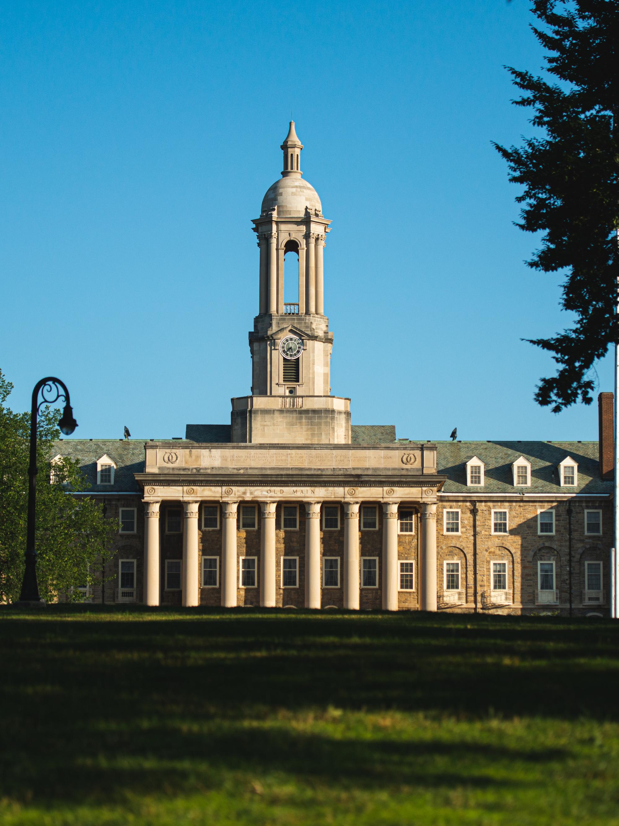Old Main at University Park campus with a green lawn and an American flag nearby