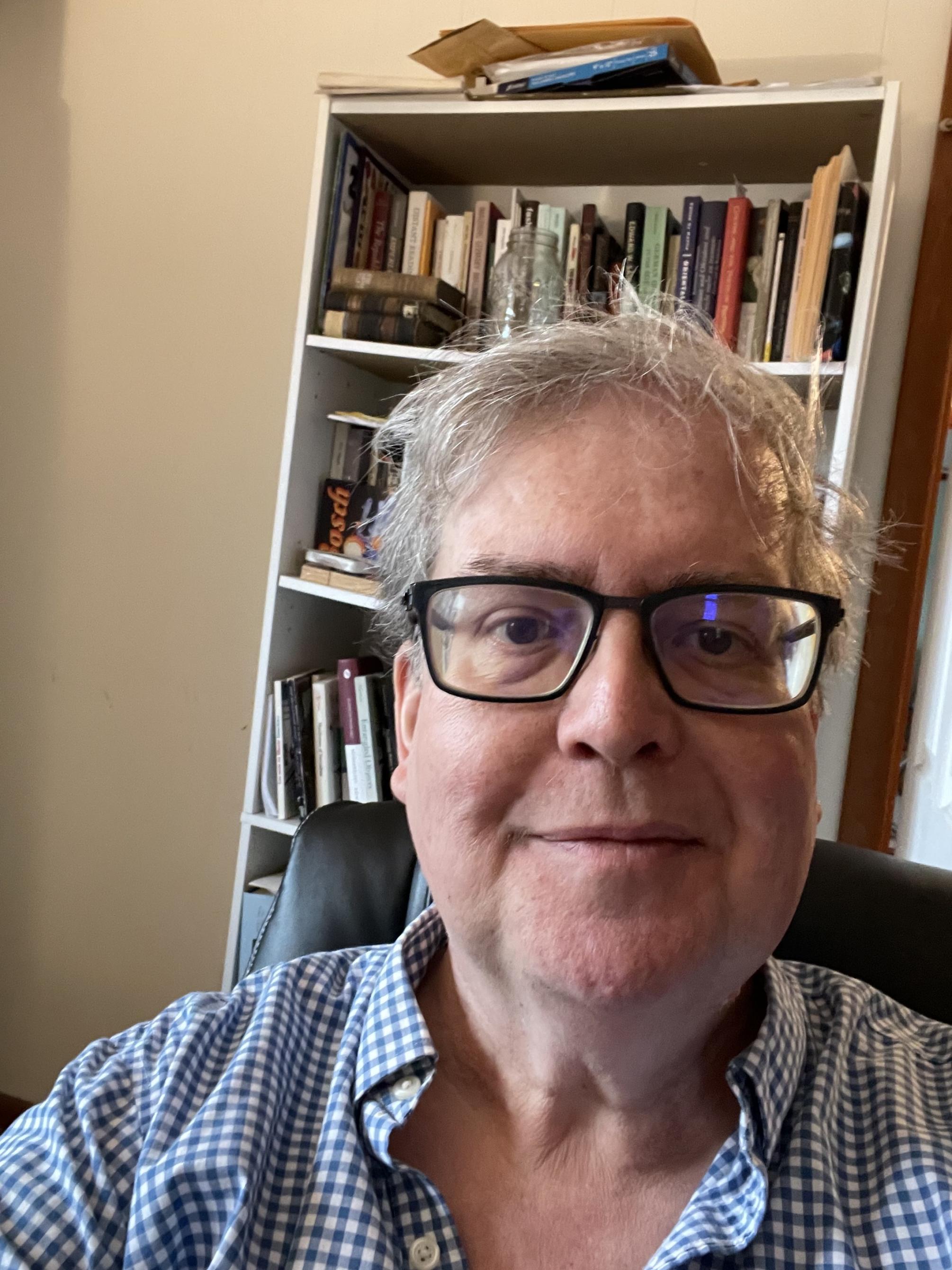 Daniel Purdy wearing checked shirt with bookcase behind him 