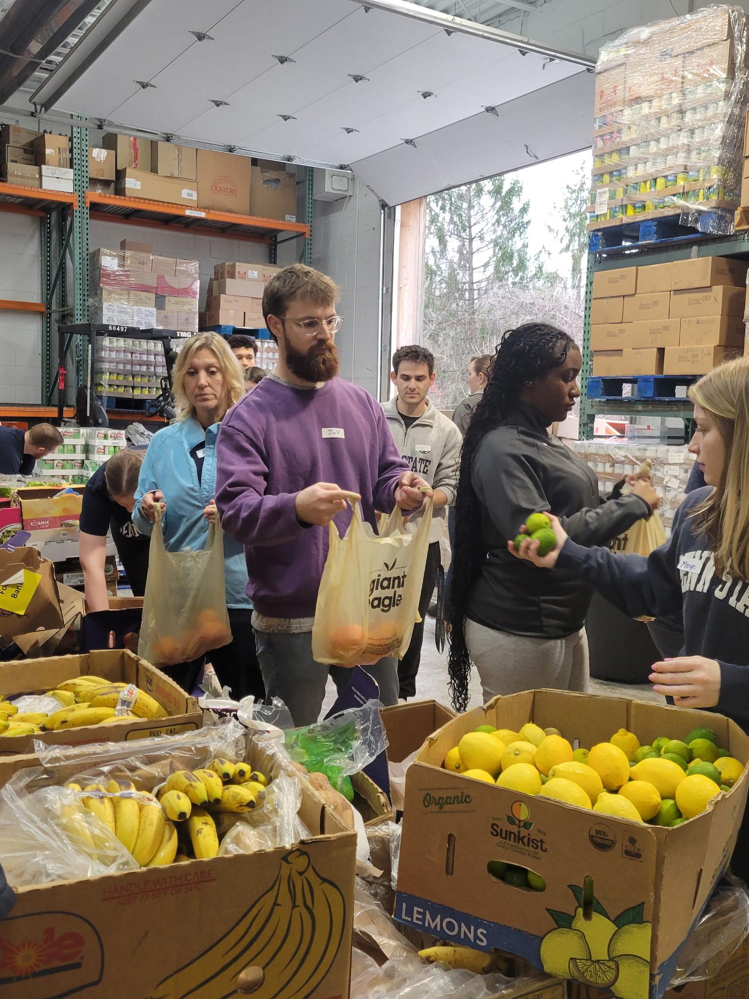People picking up produce and other items out of boxes at a food bank.