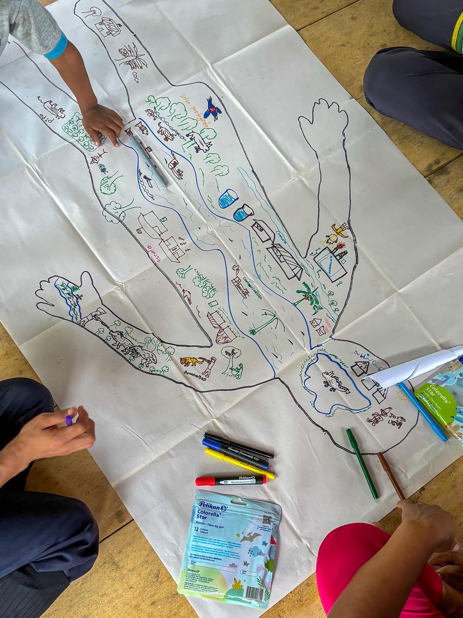 Children draw on a large paper outline of a human body, adding colorful elements like rivers, animals, and buildings.