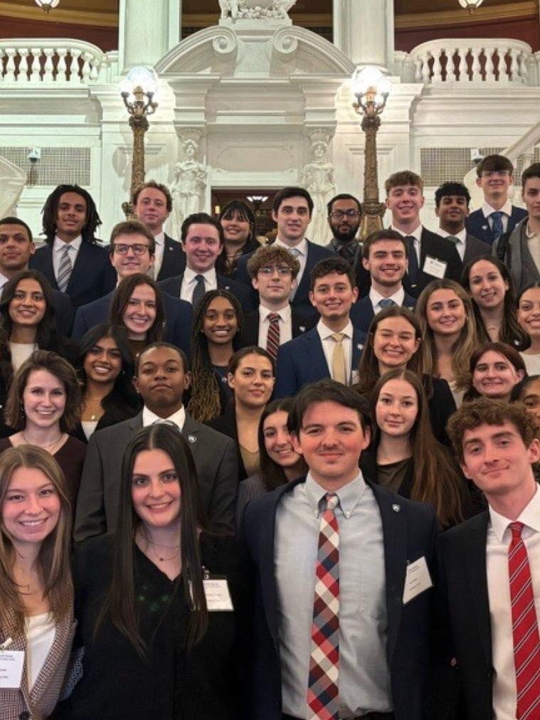 Group of professionally dressed students posing on a staircase inside a capitol building.