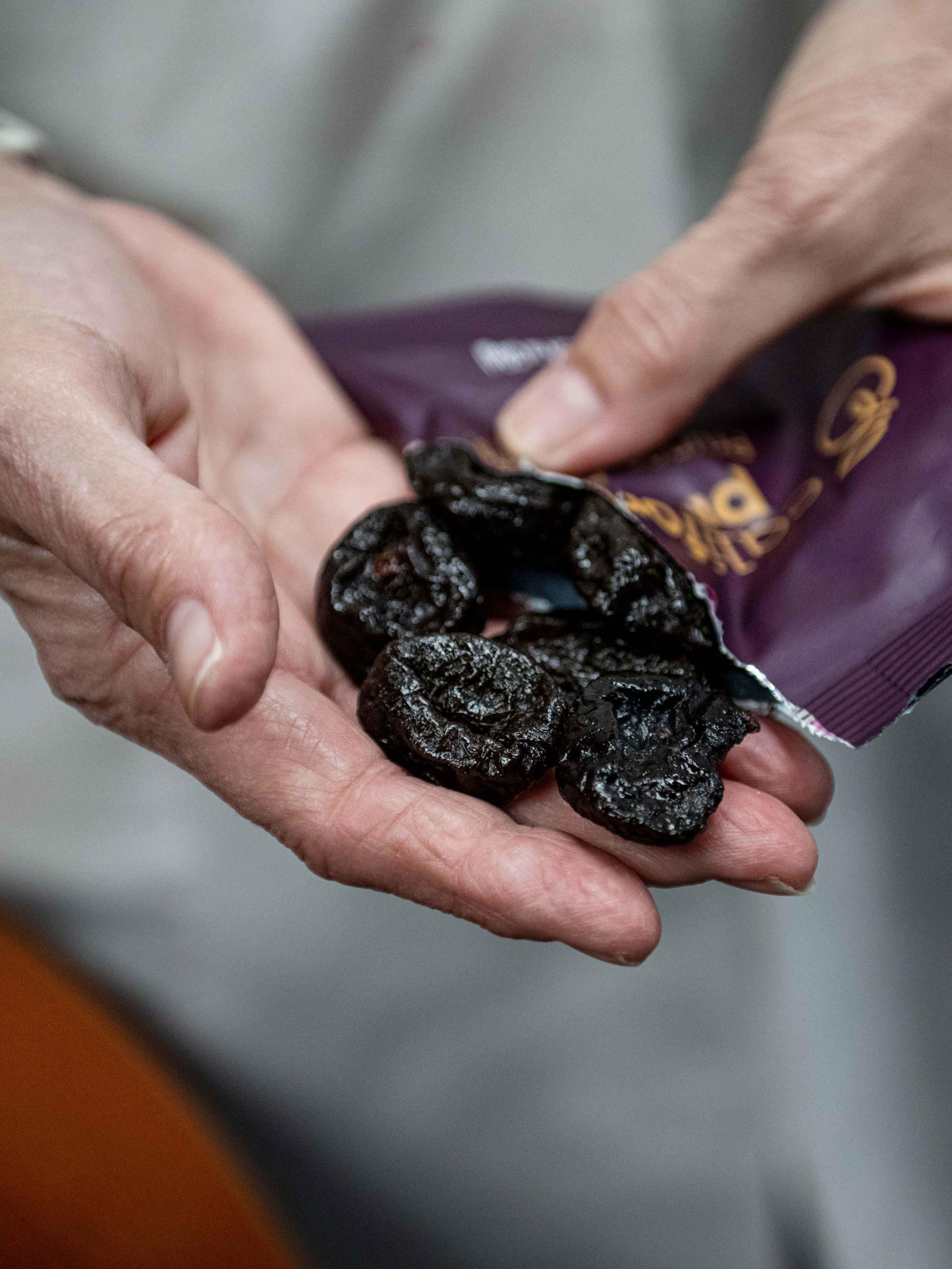An older woman's hand with six prunes in her palm