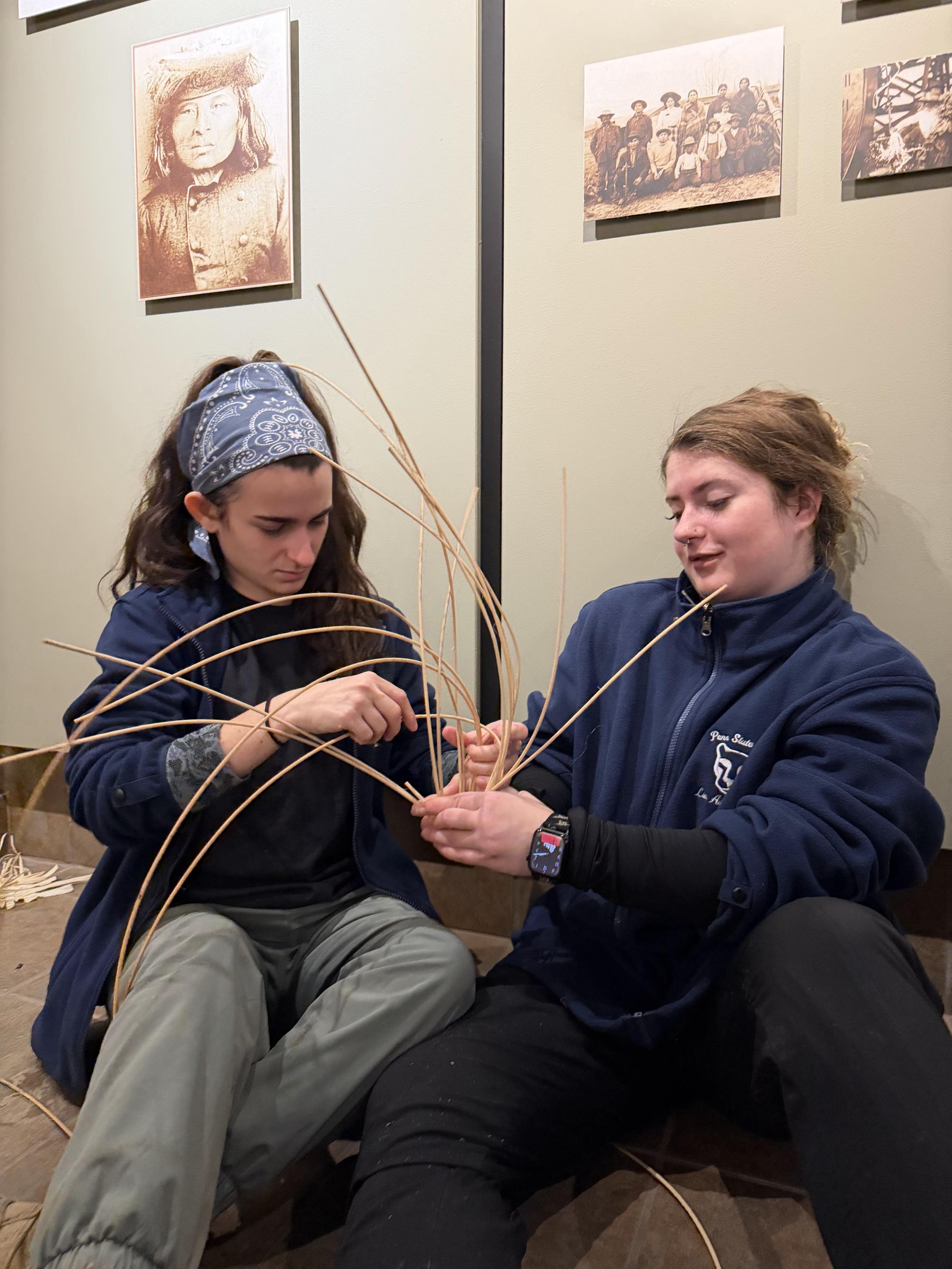 Two students weave reed together to make a basket