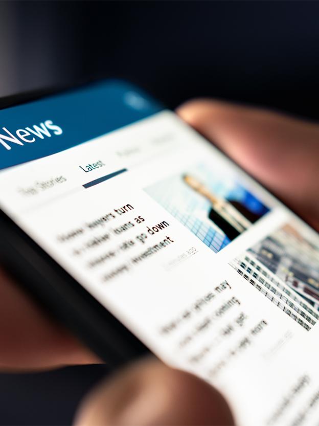 A hand holding a mobile device with a newsfeed in view.