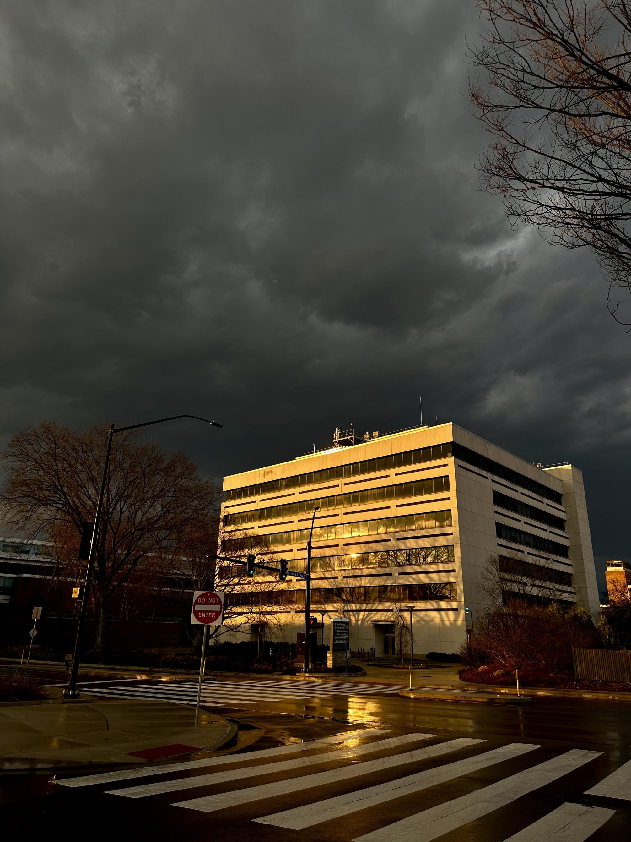 A building reflects shining sun after a spring rain, with dark gray clouds in the sky above