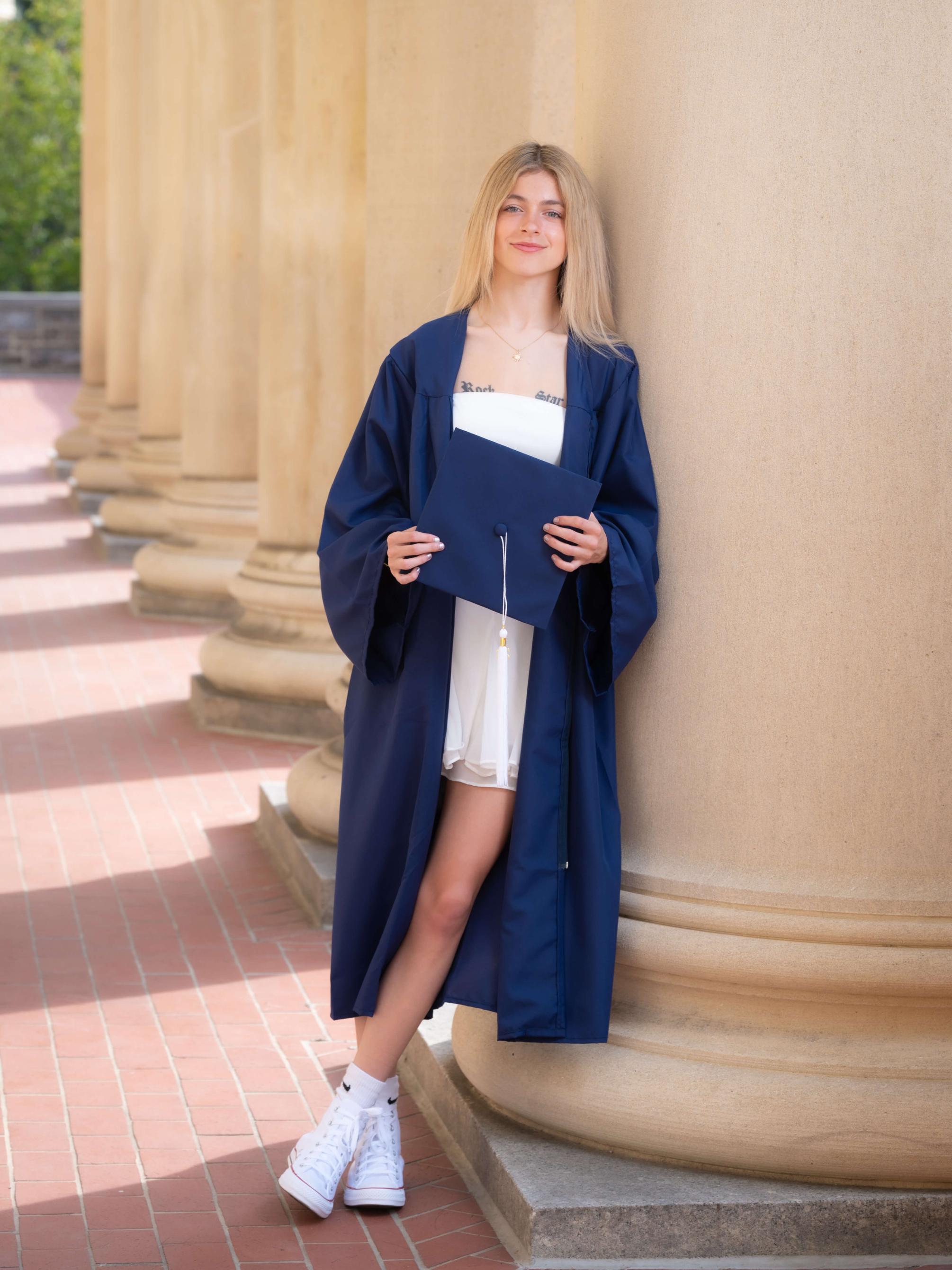 Person in a cap and gown leaning on an pillar outside of a building