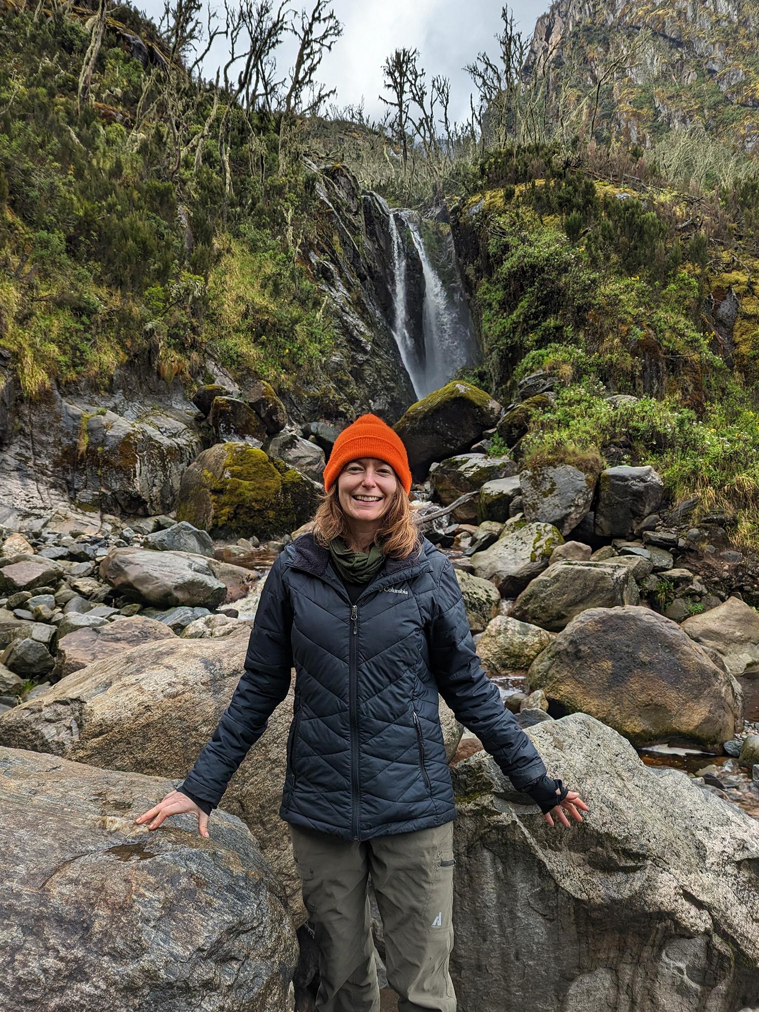 Sarah Ivory stands in front of a waterfall in the heather zone with fire damage to heather trees