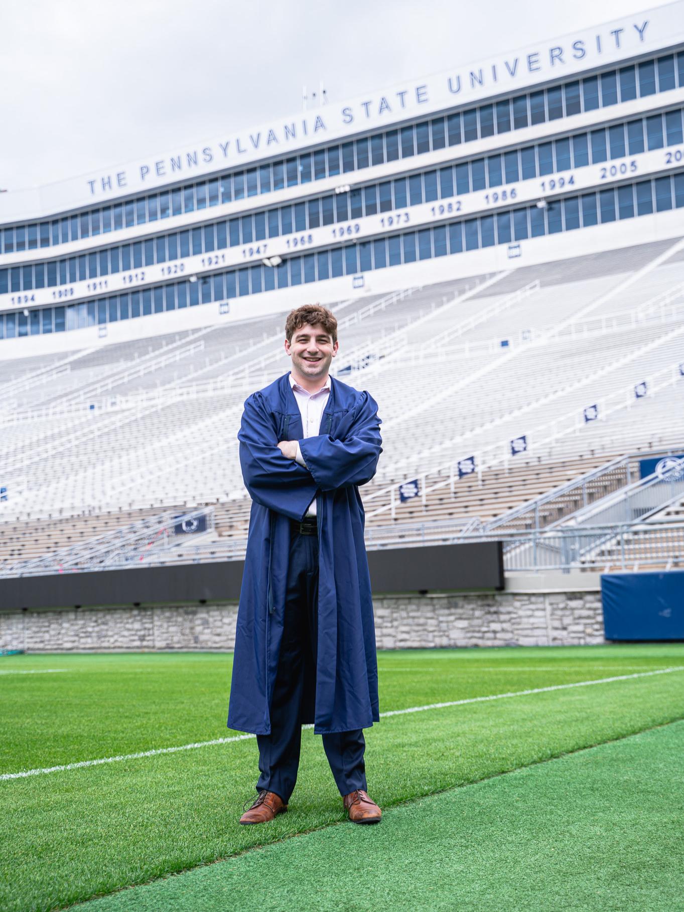 Person wearing cap and gown standing on a football field in a stadium