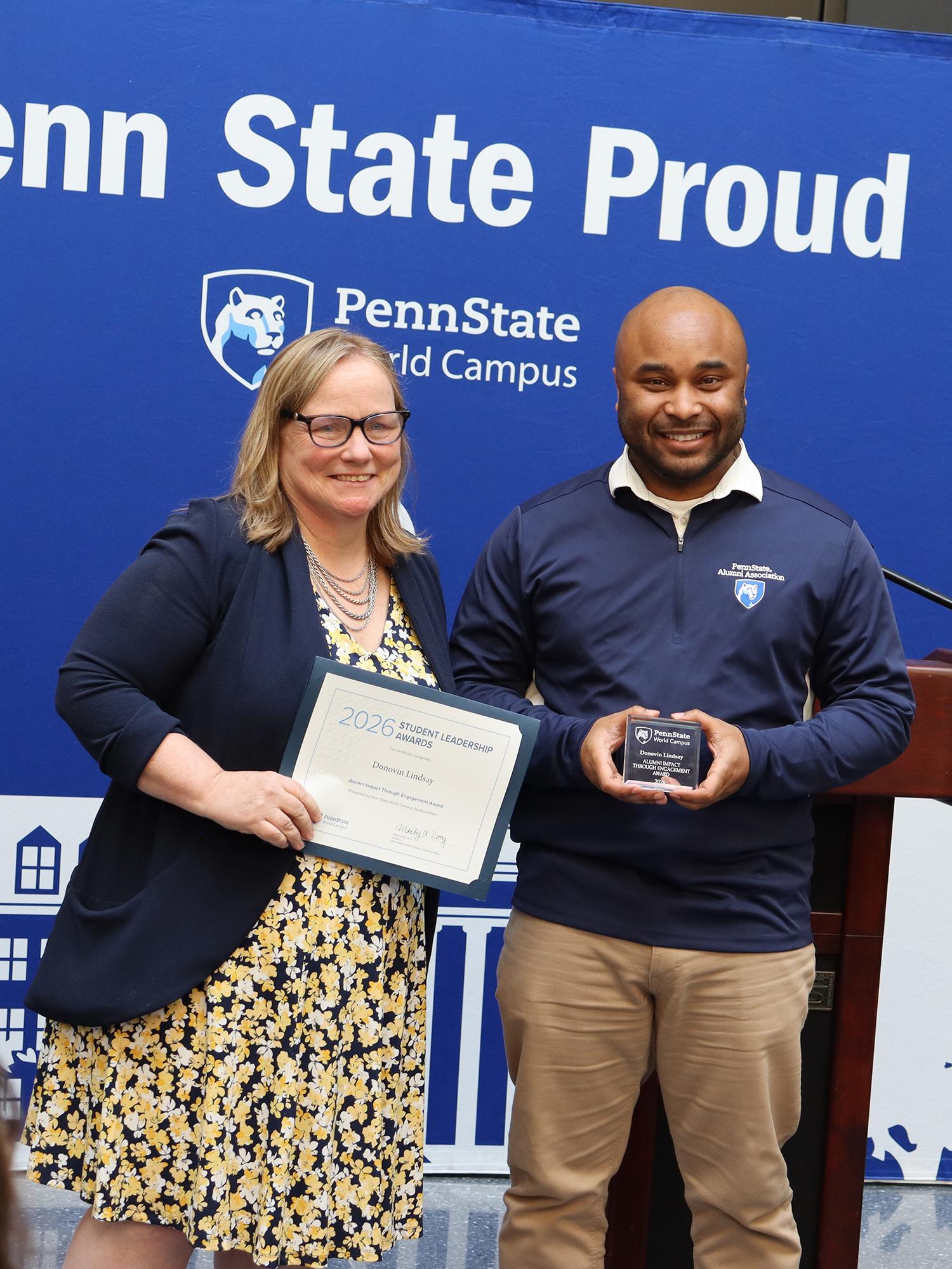 A man and a woman stand in front of a Penn State background.