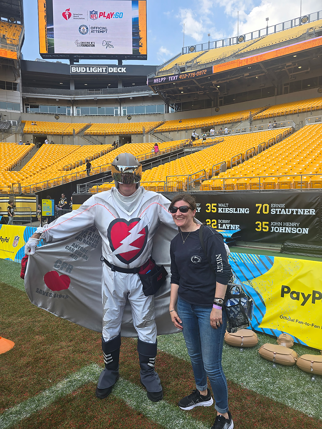 A woman stands next to a super hero on a football field.