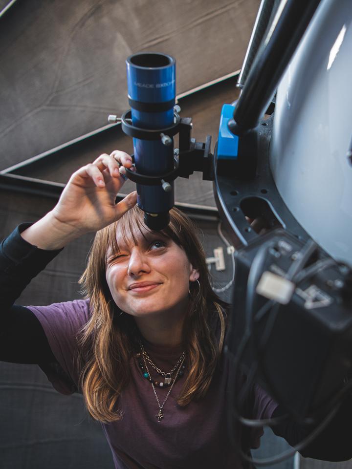 woman in purple shirt looks through telescope 