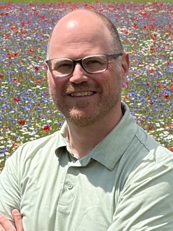 Jason Laine stands against backdrop of flowers 