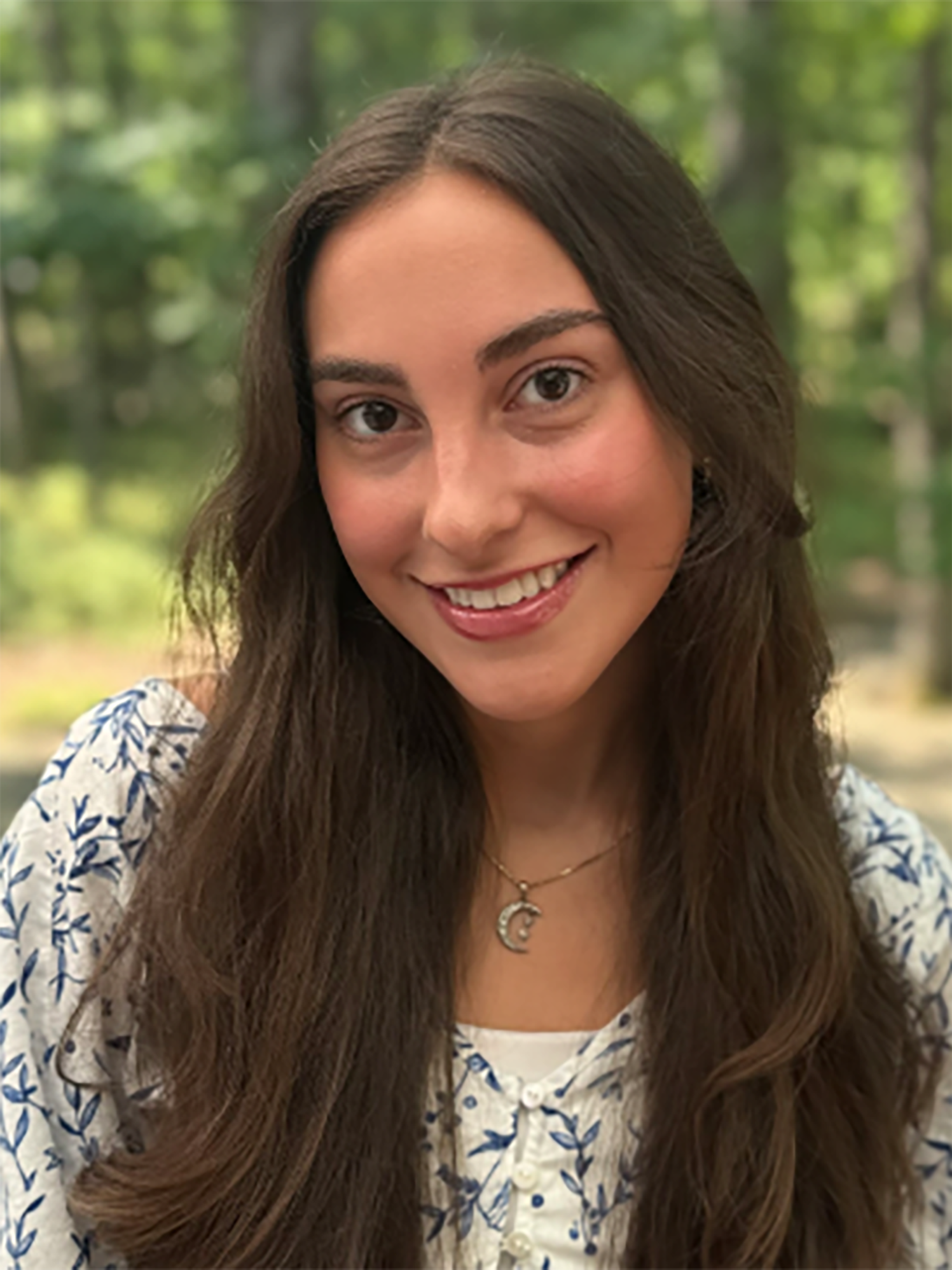 A woman wearing a floral shirt in a wooded area.