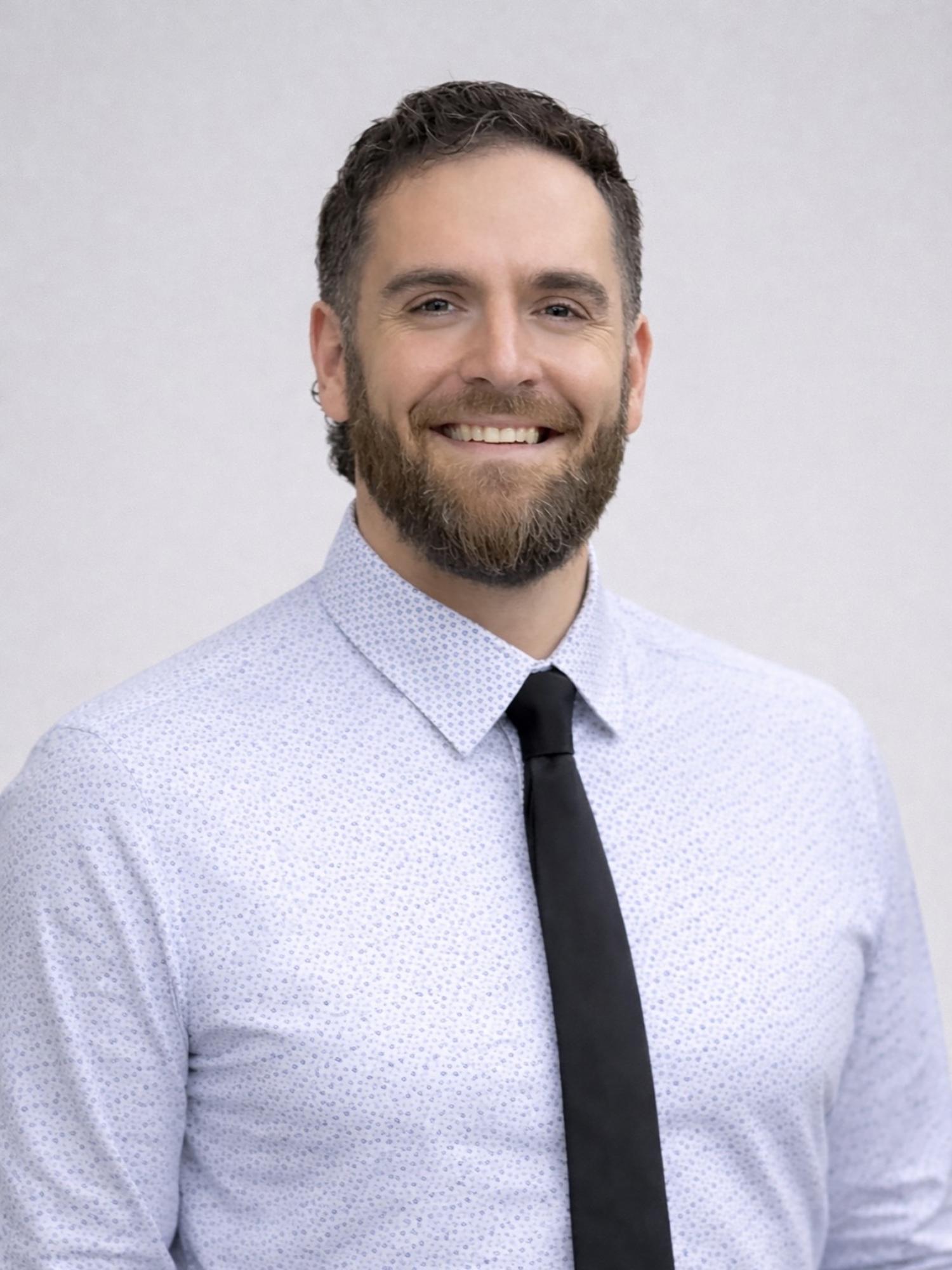 A man wearing a light dress shirt and dark tie in front of a white background.