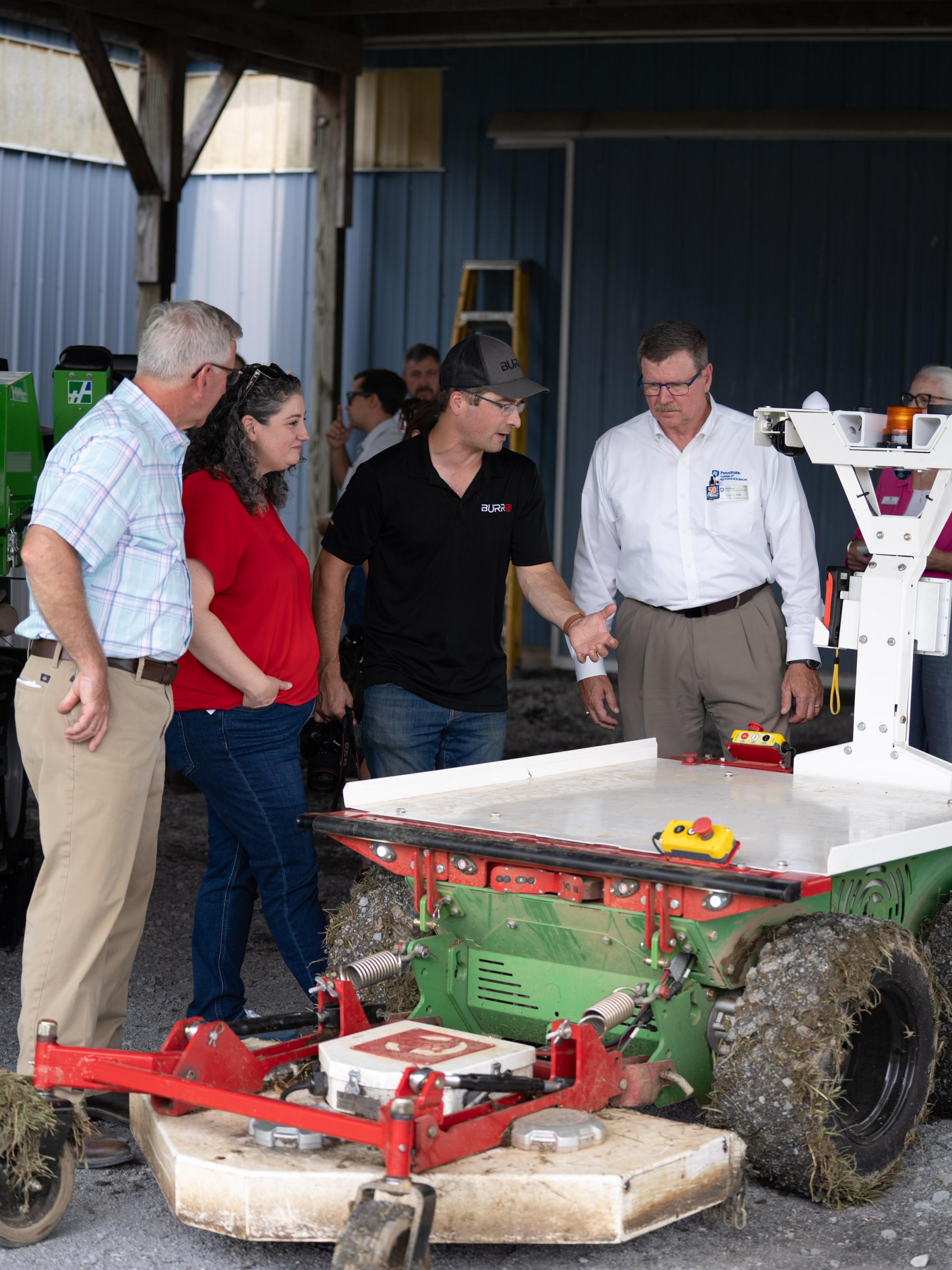 Four individuals observe a piece of agricultural innovation on top of a tractor