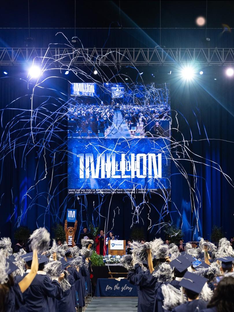 A wide shot of a commencement ceremony with streamers floating above graduates with a "1MILLION" sign in the center