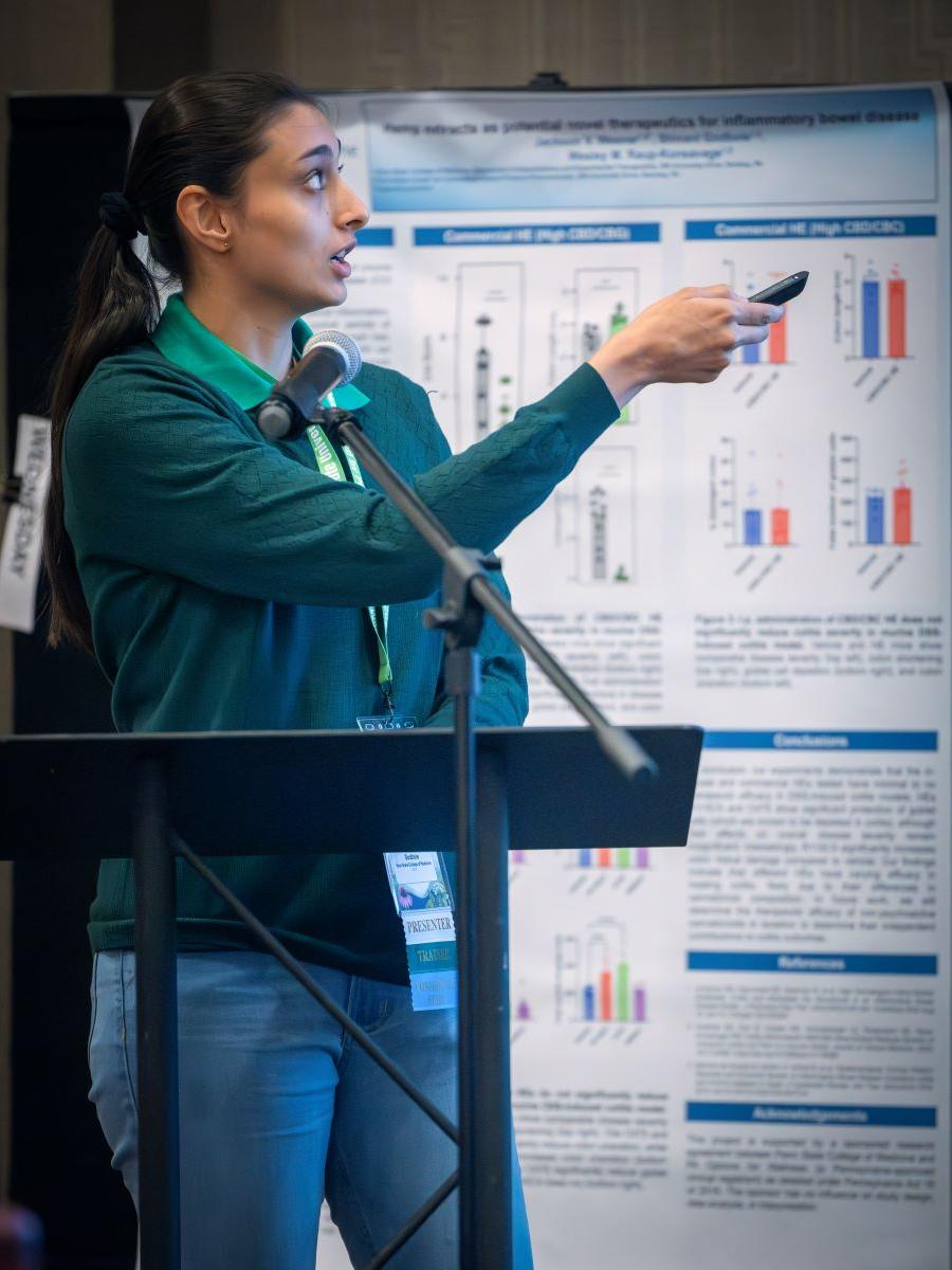 A woman stands at a podium holding a remote, pointing it toward a projector screen.
