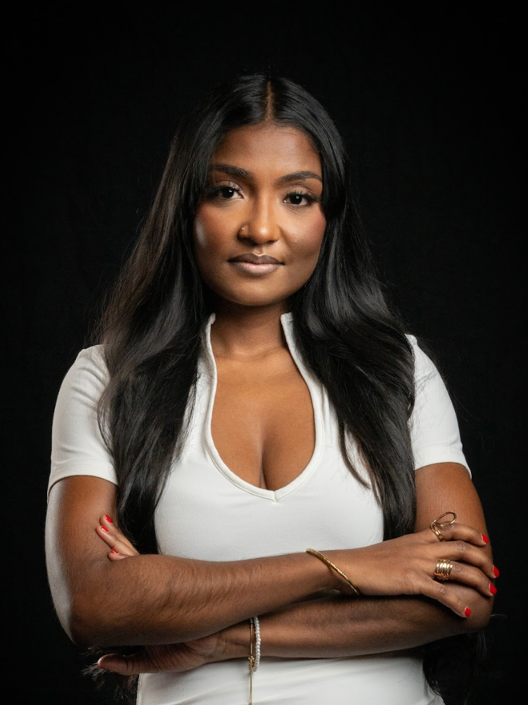 A woman of color crosses her arms and smiles.