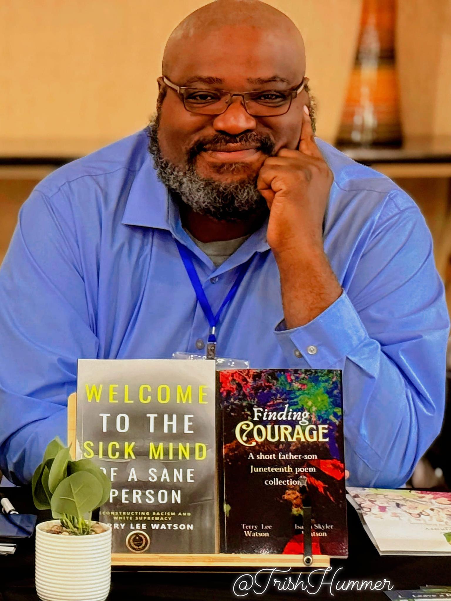 A Black man wearing glasses rests his hand on his chin.