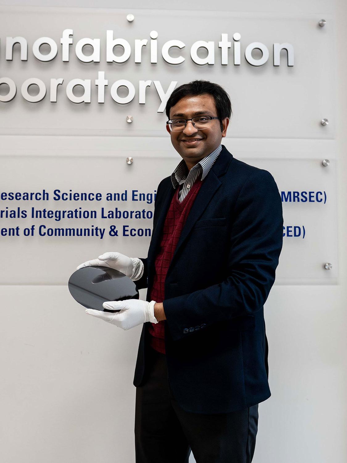 Researcher Saptarshi Das poses in front of the Nanofabrication Lab at Penn State's Materials Research Institute, smiling and holding a silicon wafer used as a foundation in circuit construction