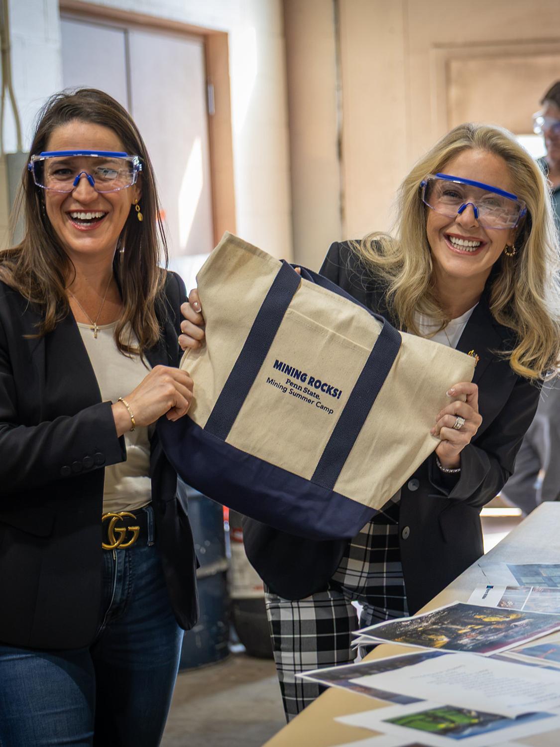 Two women in a minerals processing lab hold up a bag that says mining rocks