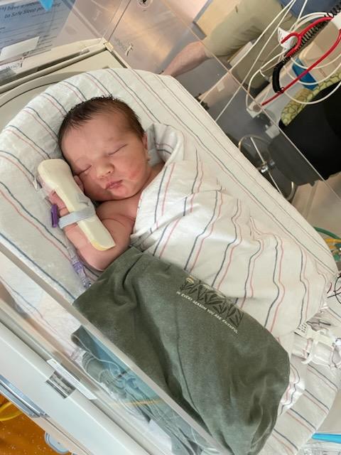 Close-up of a newborn infant sleeping in a hospital bassinet, swaddled in a white striped blanket.