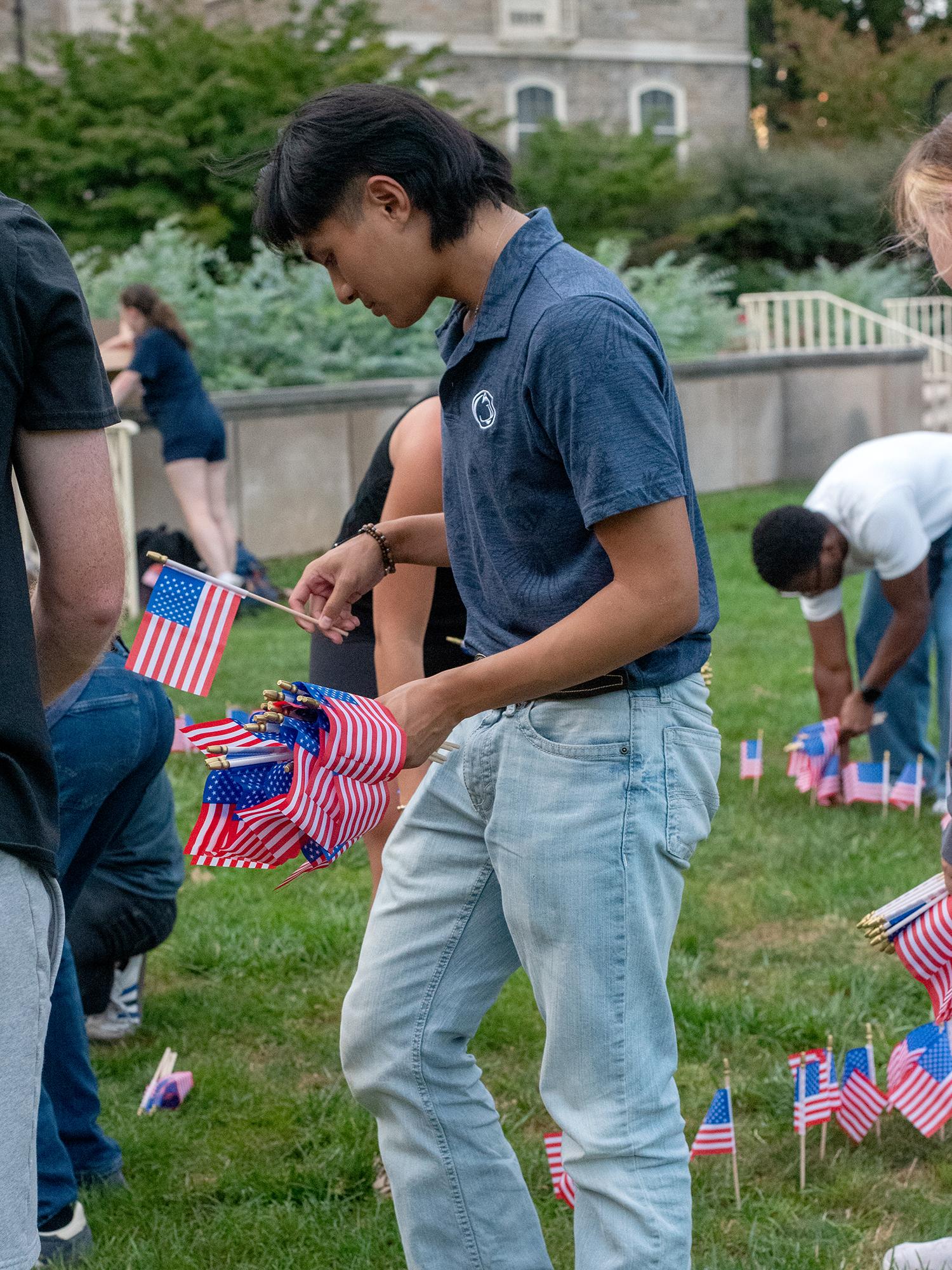 A student plants mini American flags in the grass with others around him doing the same