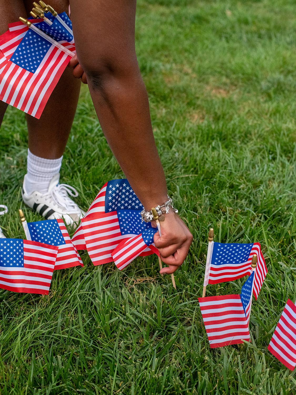 A student plants an American flag into the grass with others around it.