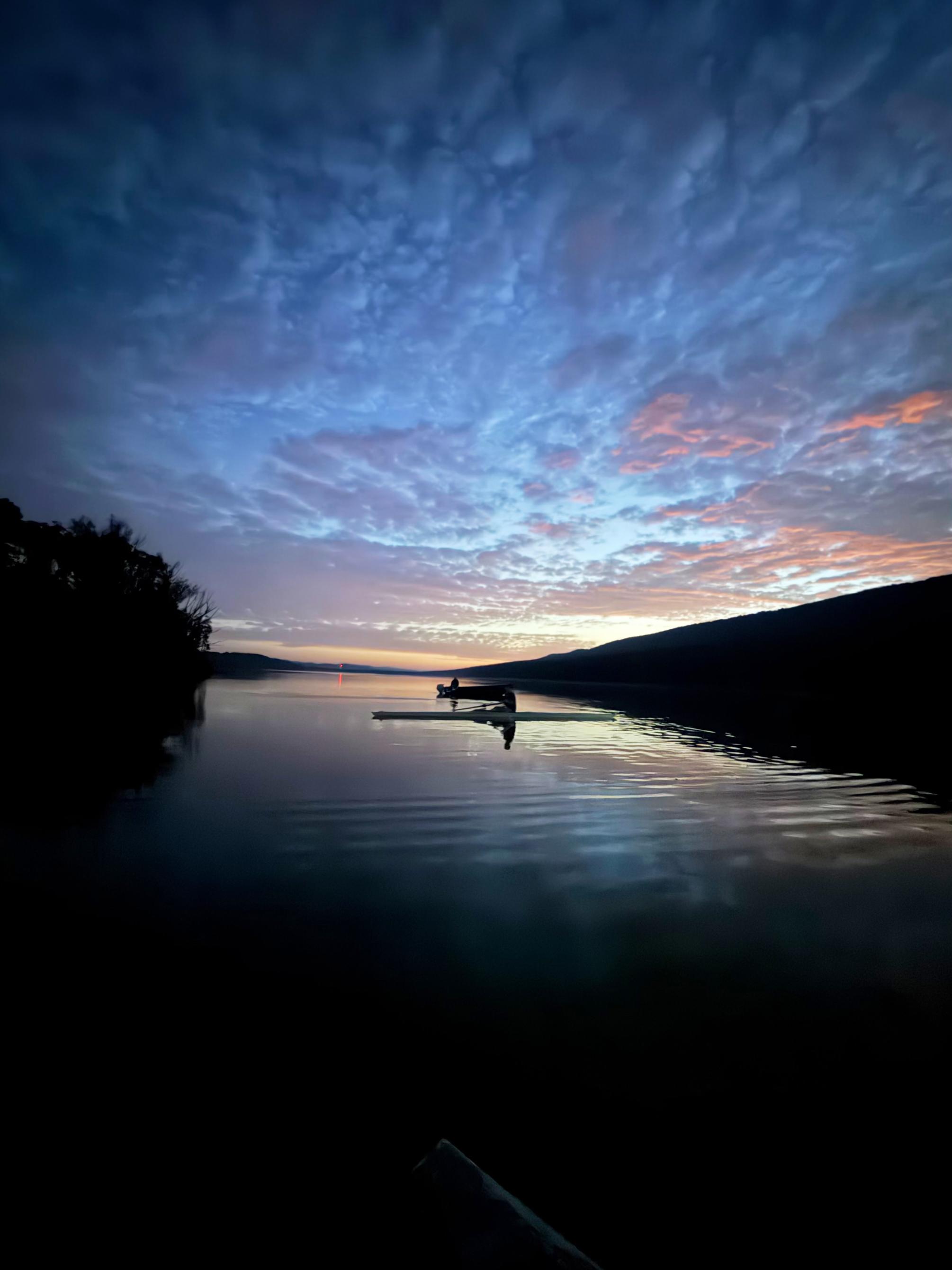 Blue and pink sunrise over a dark reservoir, with two silhouettes rowing in the center