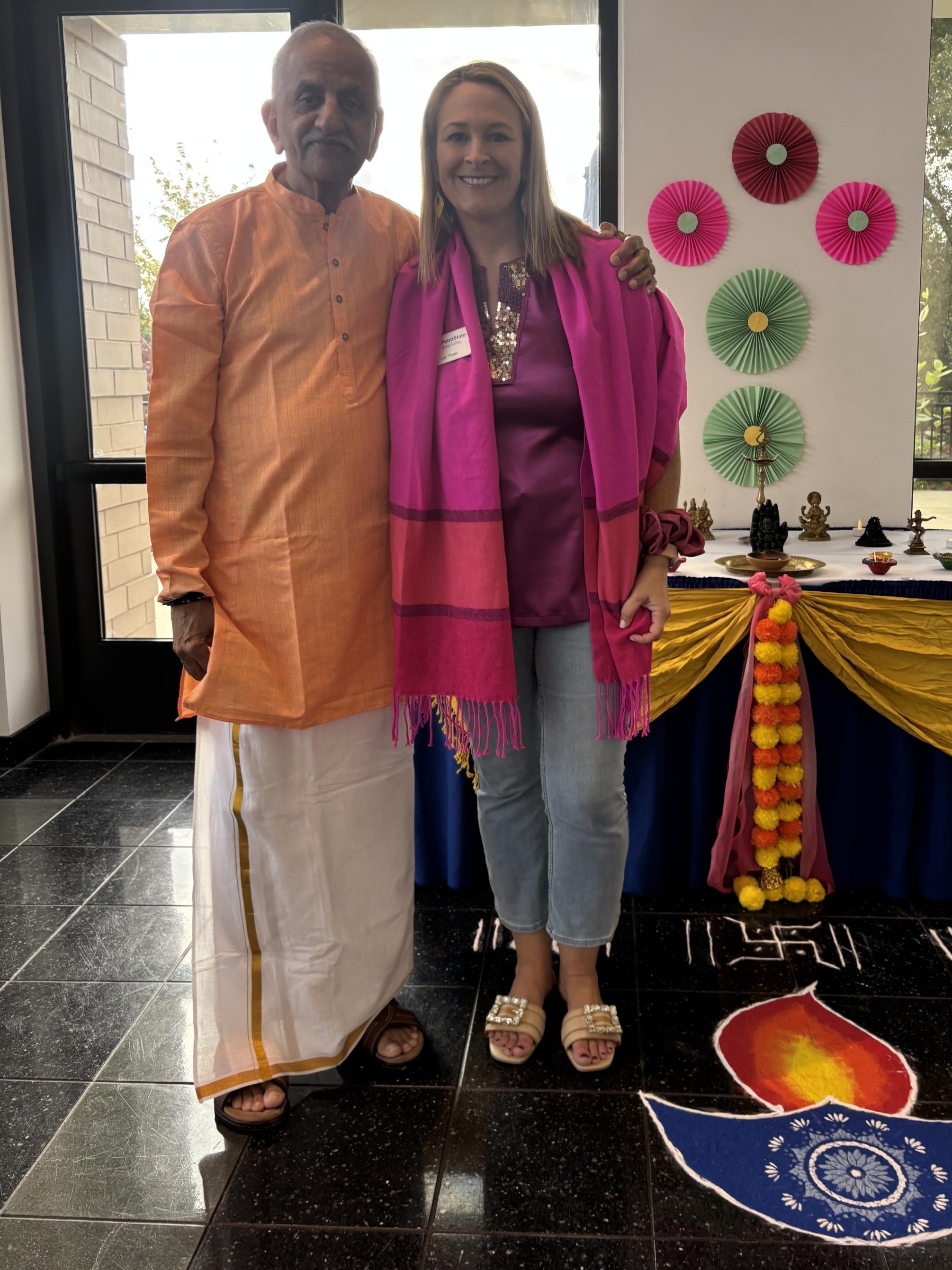 A man and a woman in festive attire stand next to Diwali decorations.
