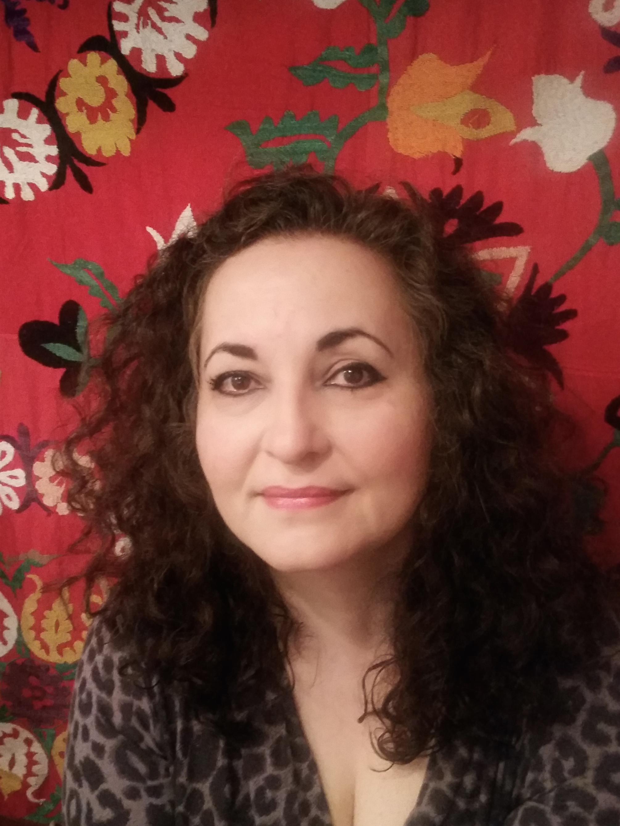 photo portrait of white woman with long, dark, curly hair in front of bold floral patterned fabric backdrop