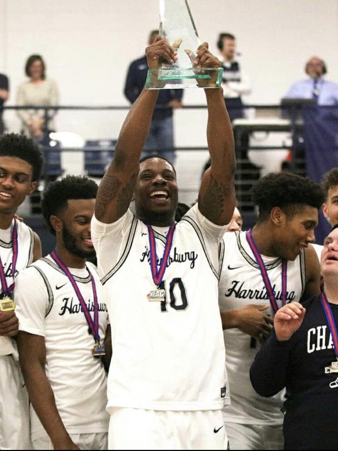Clinton Asalu, surrounded by fellow members of the men's basketball team at Penn State Harrisburg, holds up a trophy in celebration