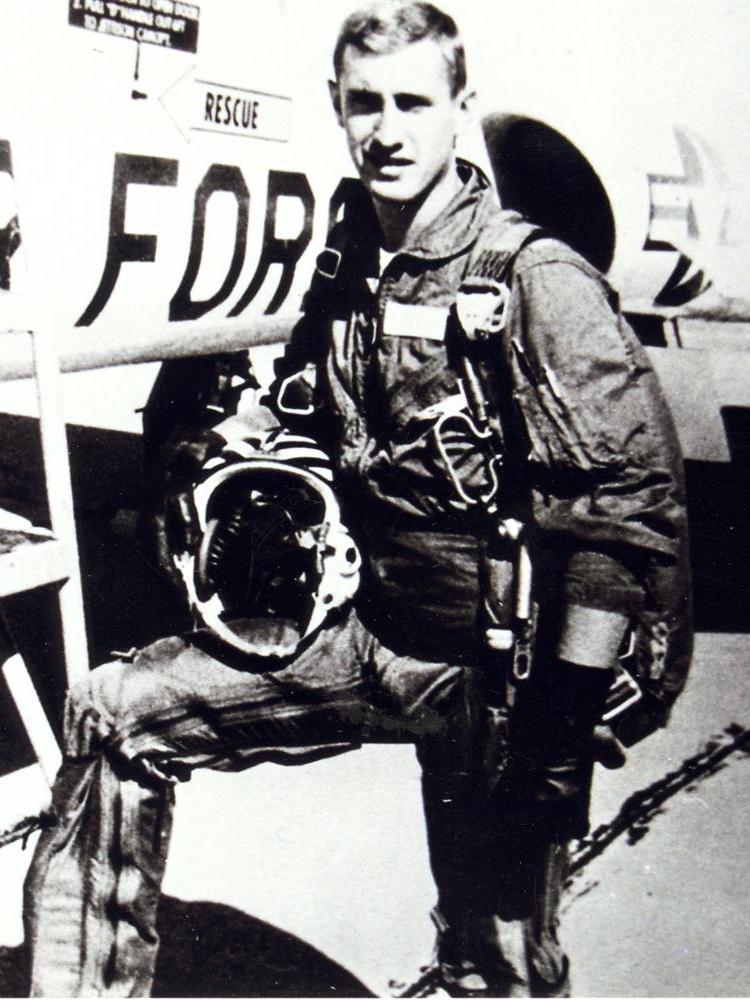 A military service member stands outside of a plane in gear.