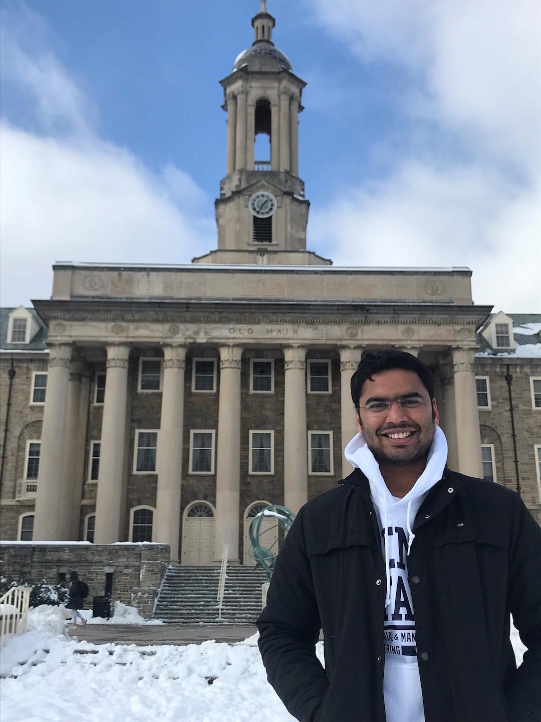 Man in black jacket stands in front of the Old Main building on the University Park campus.