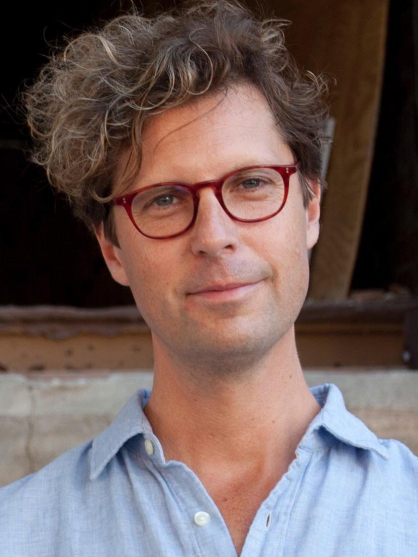 A man wearing glasses and shown from the shoulders up smiles.