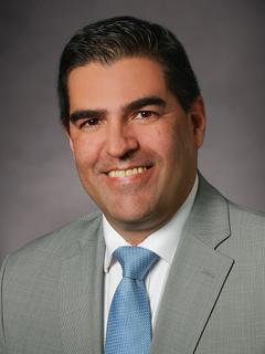 A posed portrait of a smiling man in front of a grey backdrop